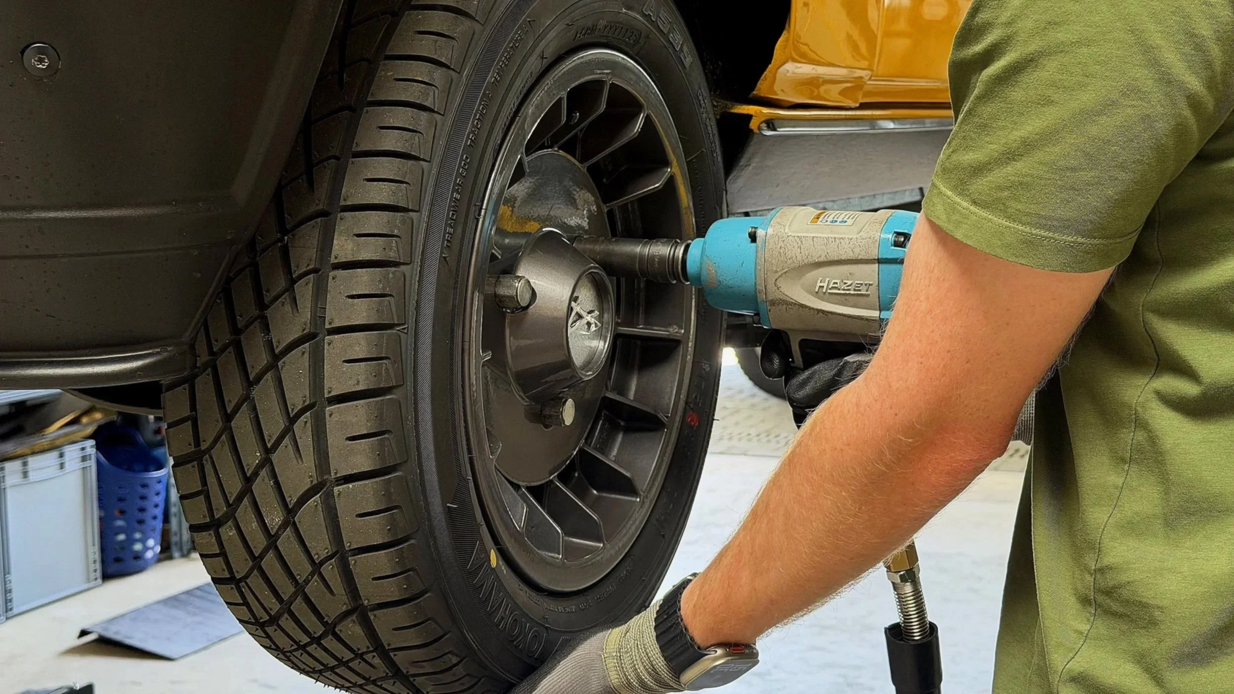 Person wechselt einen Autoreifen mit einem elektrischen Werkzeug auf einer Hebebühne in der Werkstatt.