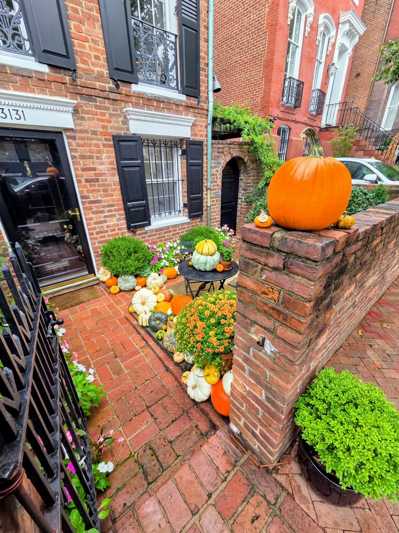 Brick front porch decorated with multiple pumpkins and flowers.