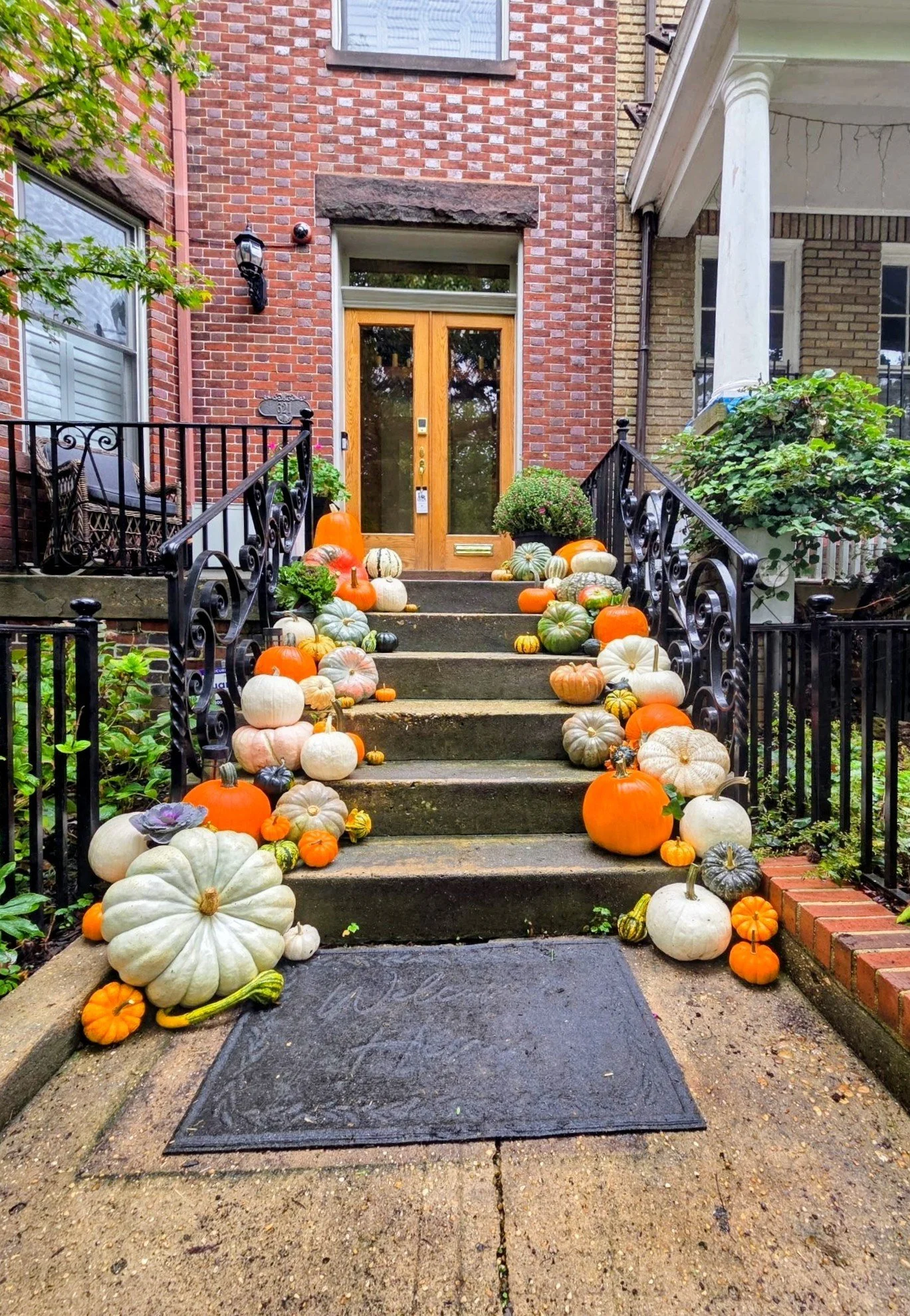 Front porch of a brick house decorated with a large collection of colorful pumpkins and gourds along the steps leading to the front door.