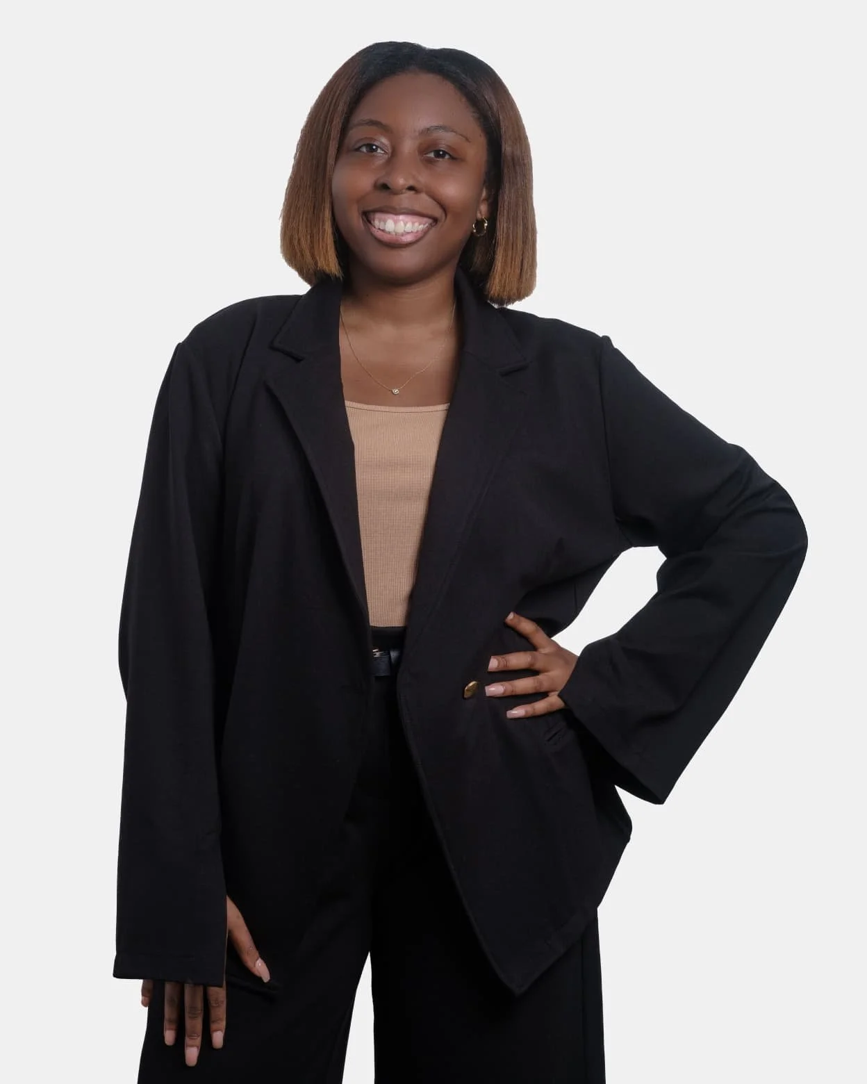 A woman smiling with one hand on her hip, wearing a black blazer, beige top, and black pants, standing against a plain white background.