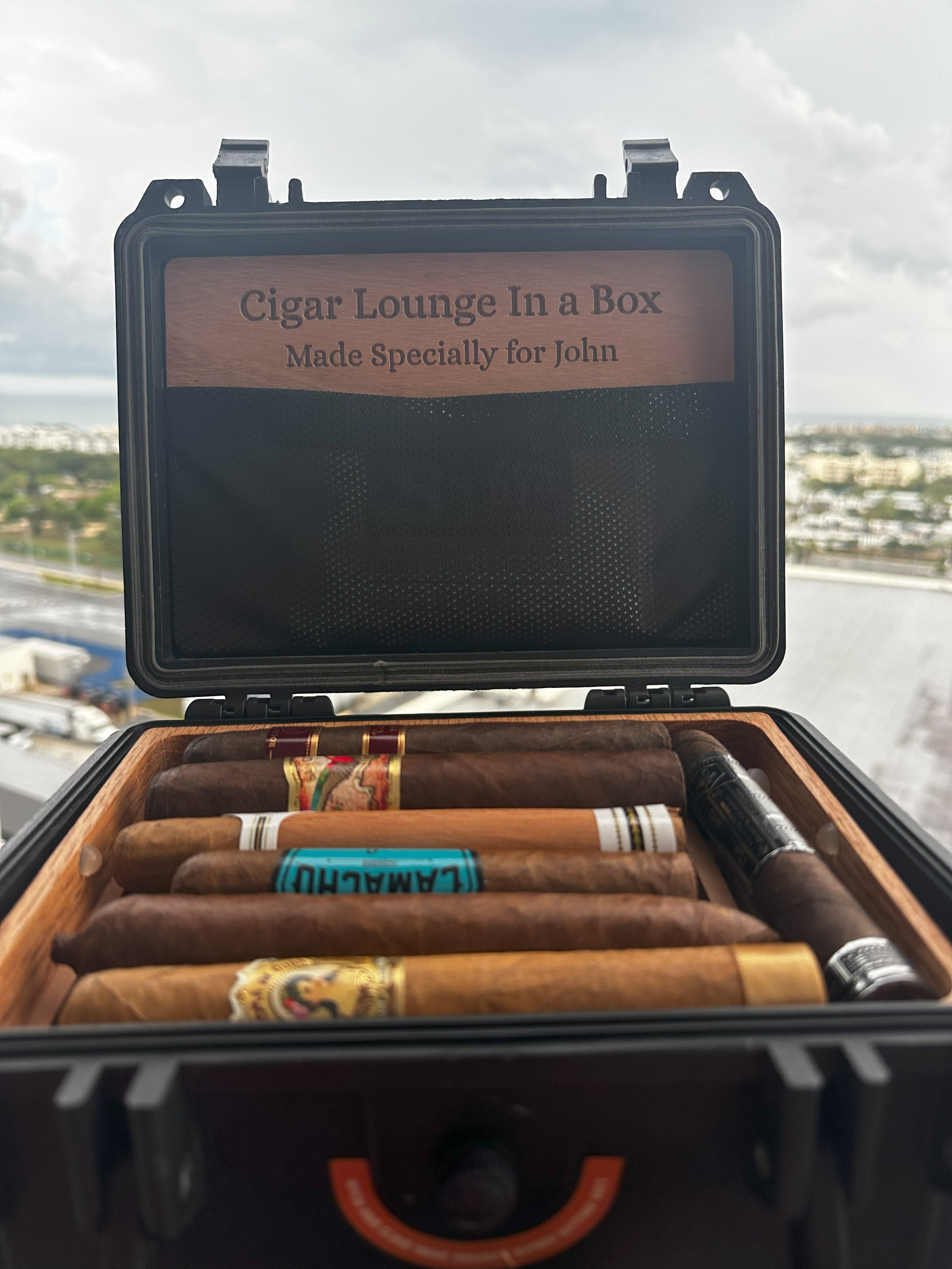 Open cigar box labeled 'Cigar Lounge in a Box Made Specially for John,' containing cigars of various sizes and bands.