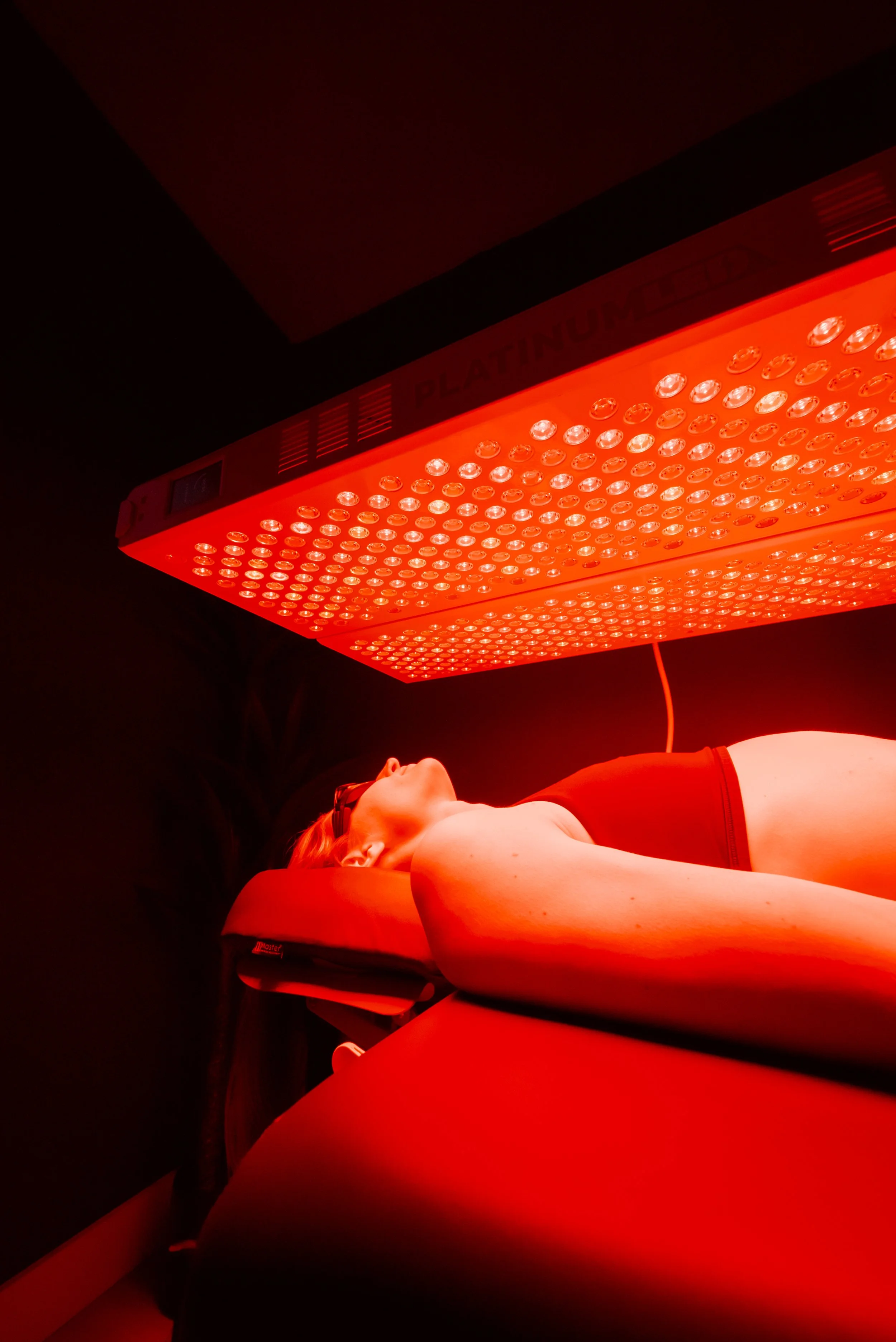 A woman in a sports bra undergoing red light therapy treatment in a wellness center.