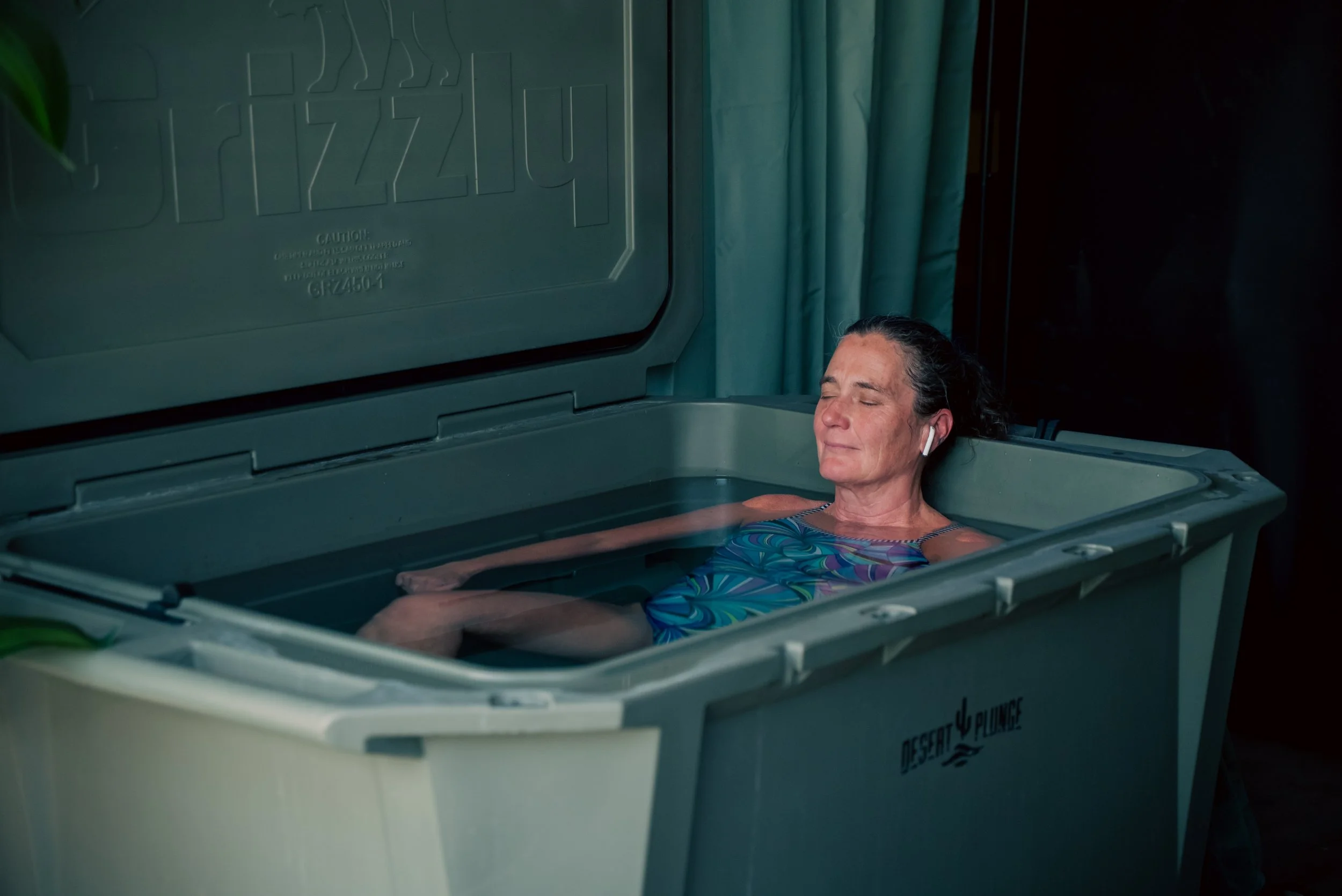 Two people relaxing in an insulated cooler filled with water, Cold Plunge for two, branded 'Desert Plunge', on a plain white background.