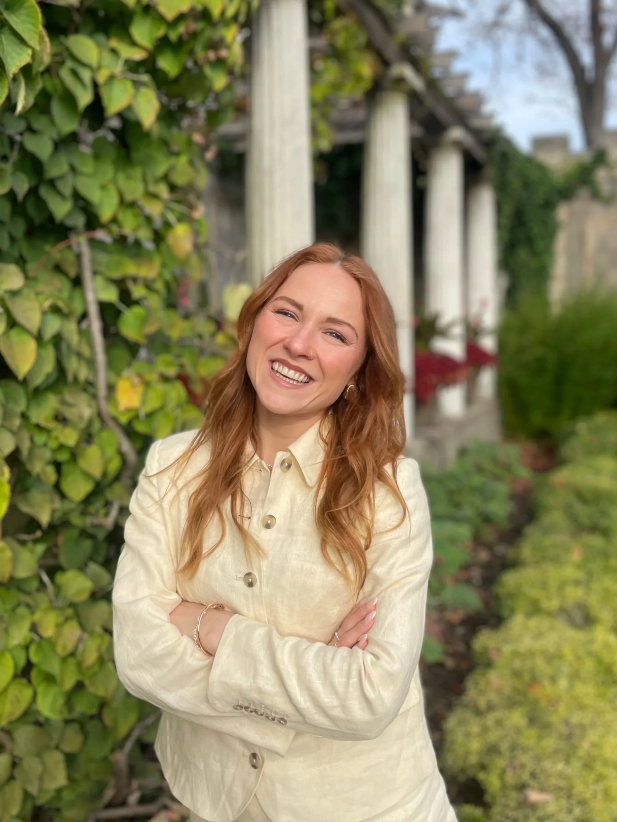 Person sitting on a wooden bench wearing a denim outfit, outdoors with lush greenery in the background.