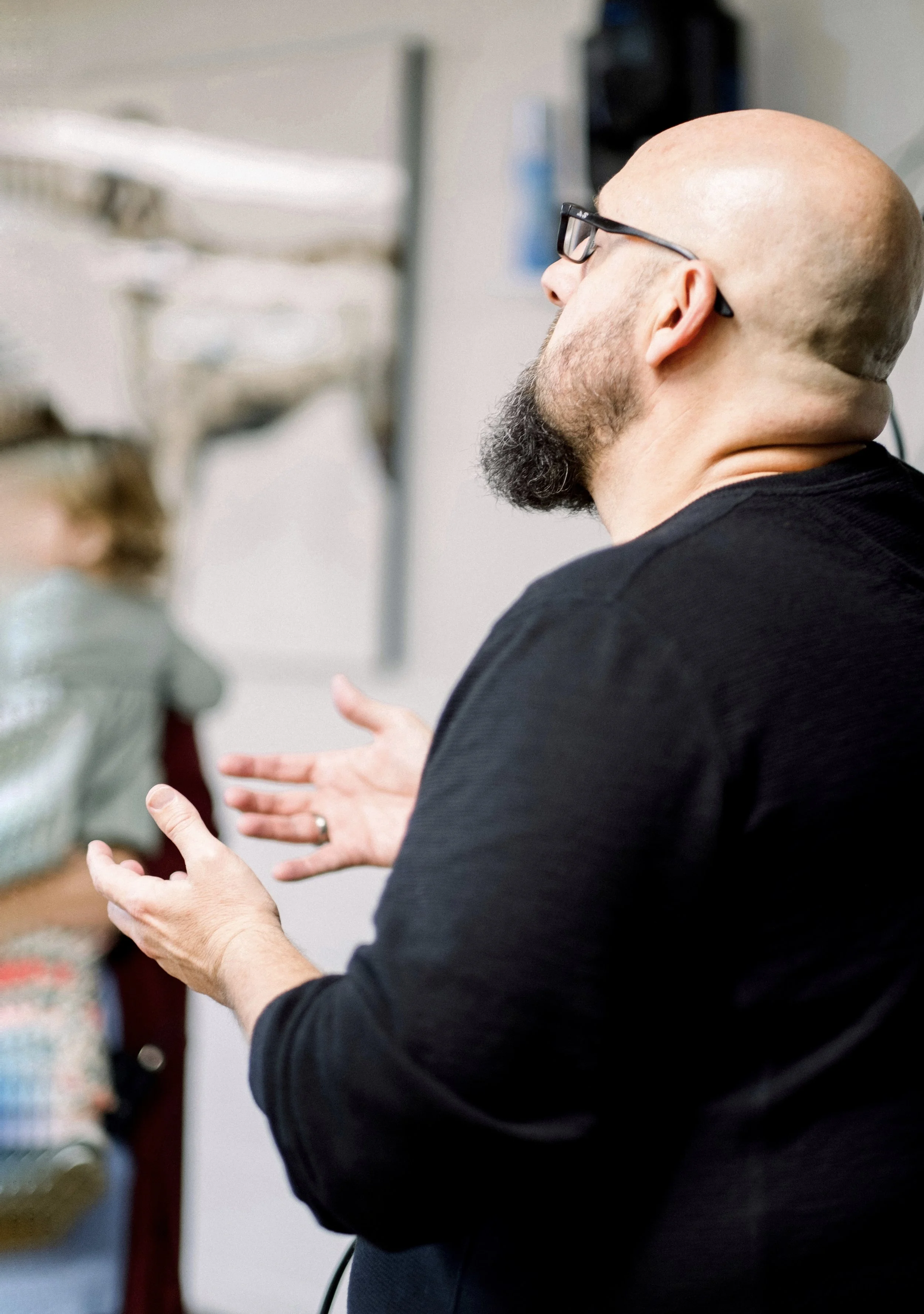 A bald man with a beard wearing glasses and a black shirt praying and worshiping God