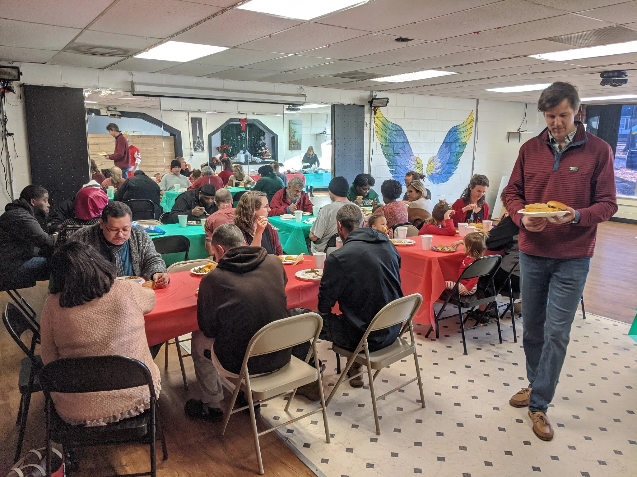 A christmas party with many members gathering around a table with food and laughing and talking