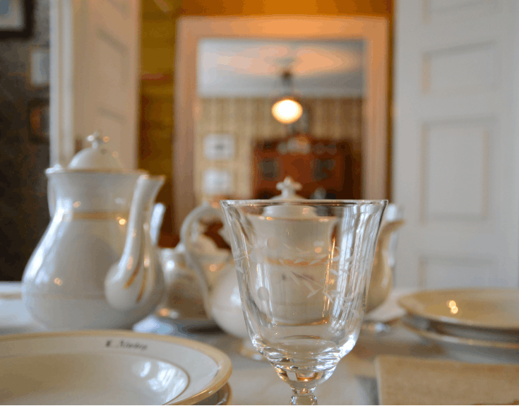 En glass, noen hvite serviser og tekanner på et bord i et rom med trevegger og lofte.