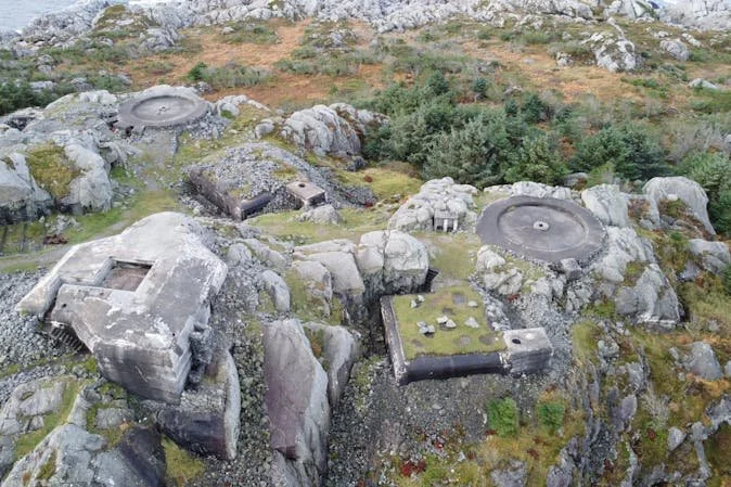 En ødelagt militærbase på risikabel beliggenhet i fjellterreng, med betongkonstruksjoner og overvokste områder.