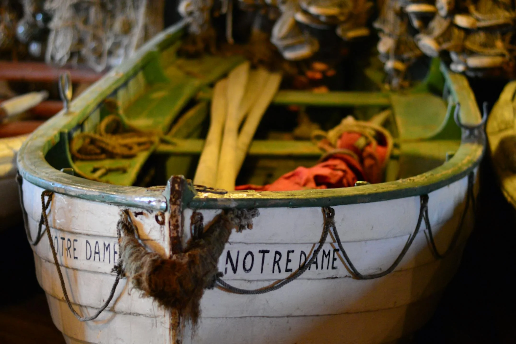 A gammel, hvit jernbåt med rustne detaljer og påskriften "NOTRE DAME" på utsiden. Inni båten ligger det noen lange grønne og røde materialer, og det er tau og en pels på utsiden.