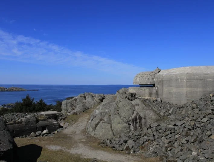 Kystlinje med store steiner og en betongstruktur mot havet under en klar blå himmel.