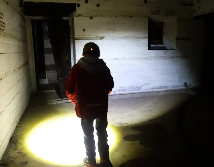 Person står inne i et tomt rom med trekledning, med lommelykt som kaster lys på gulvet