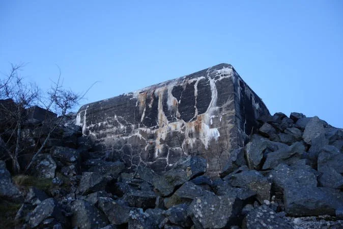 En stor, forlatt betongbunkers på en steinete fjellskrent mot en klar, blå himmel.