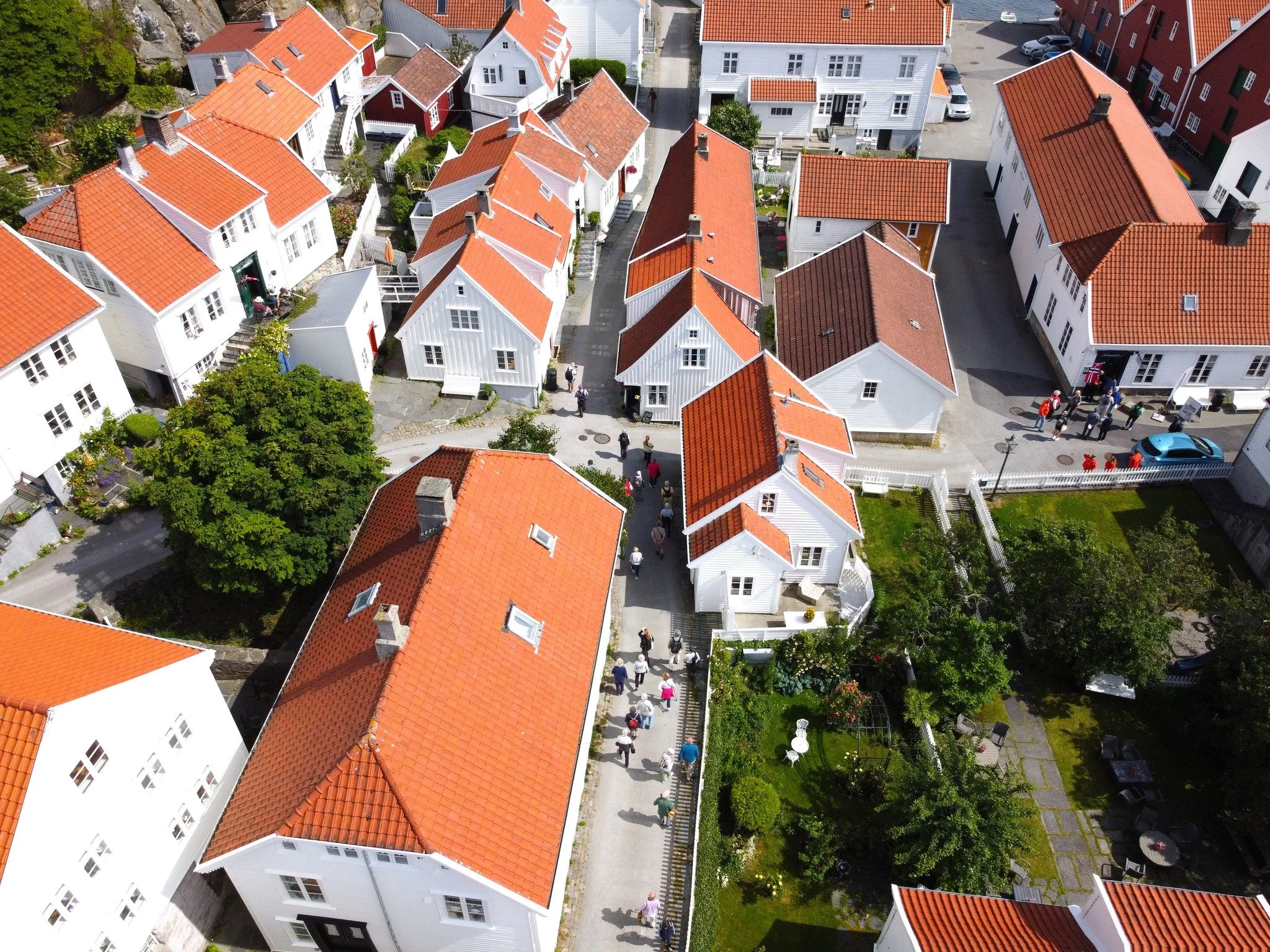 Fargerike hus med røde tak sett fra luften, med mennesker som går langs en gate og små grønne områder.