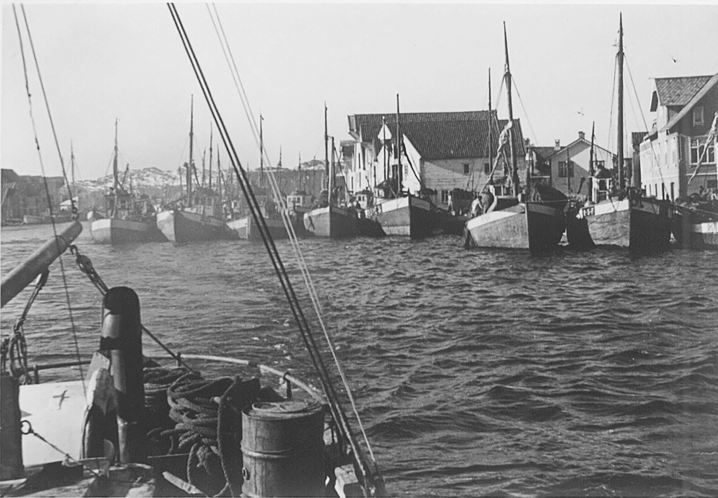 Søvnære bilder av båter i en havn med hus i bakgrunnen, tatt i svart-hvitt.