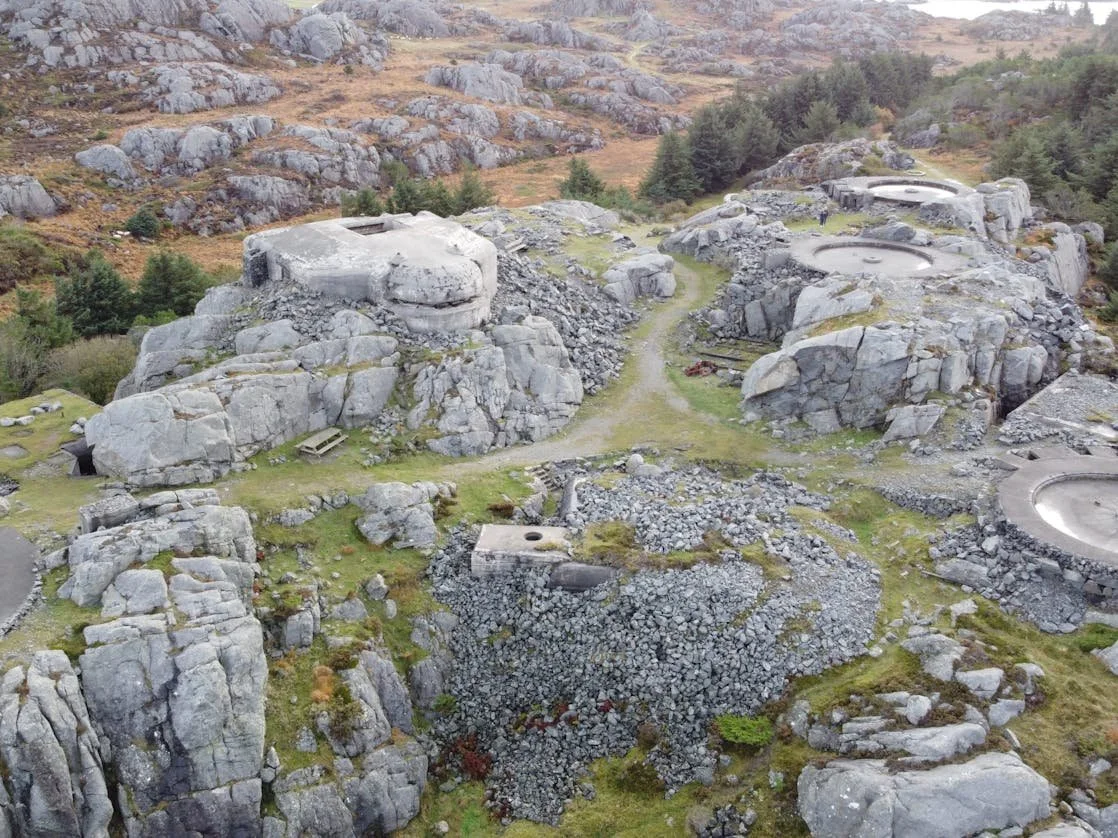 Et landskap med store steiner og jordhytter, omgitt av fjell og skog, i et kupert område.
