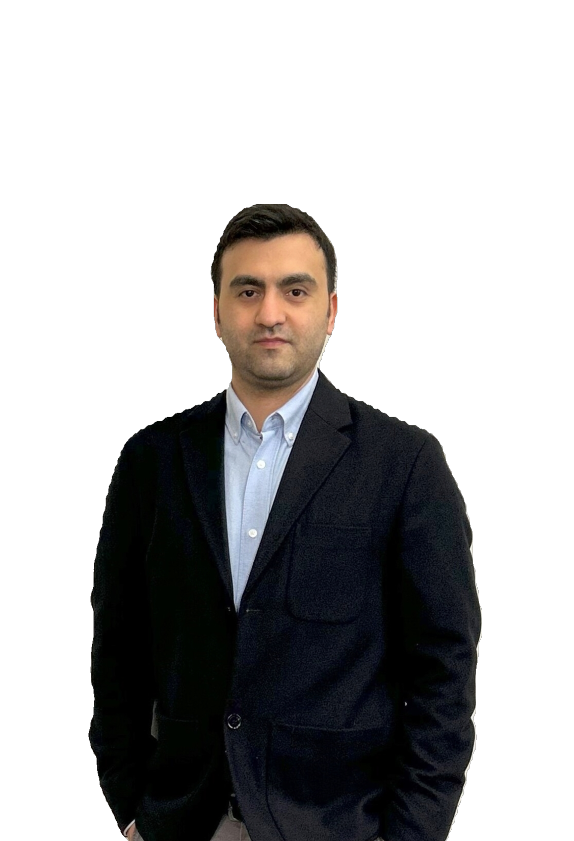 A man with dark hair and light skin wearing a dark blazer and a light blue shirt, standing against a black background.