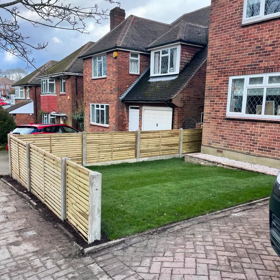 A small, neatly front yard in Orpington featuring a patch of green grass enclosed by a newly installed wooden fence and a small gravel area along the house wall.