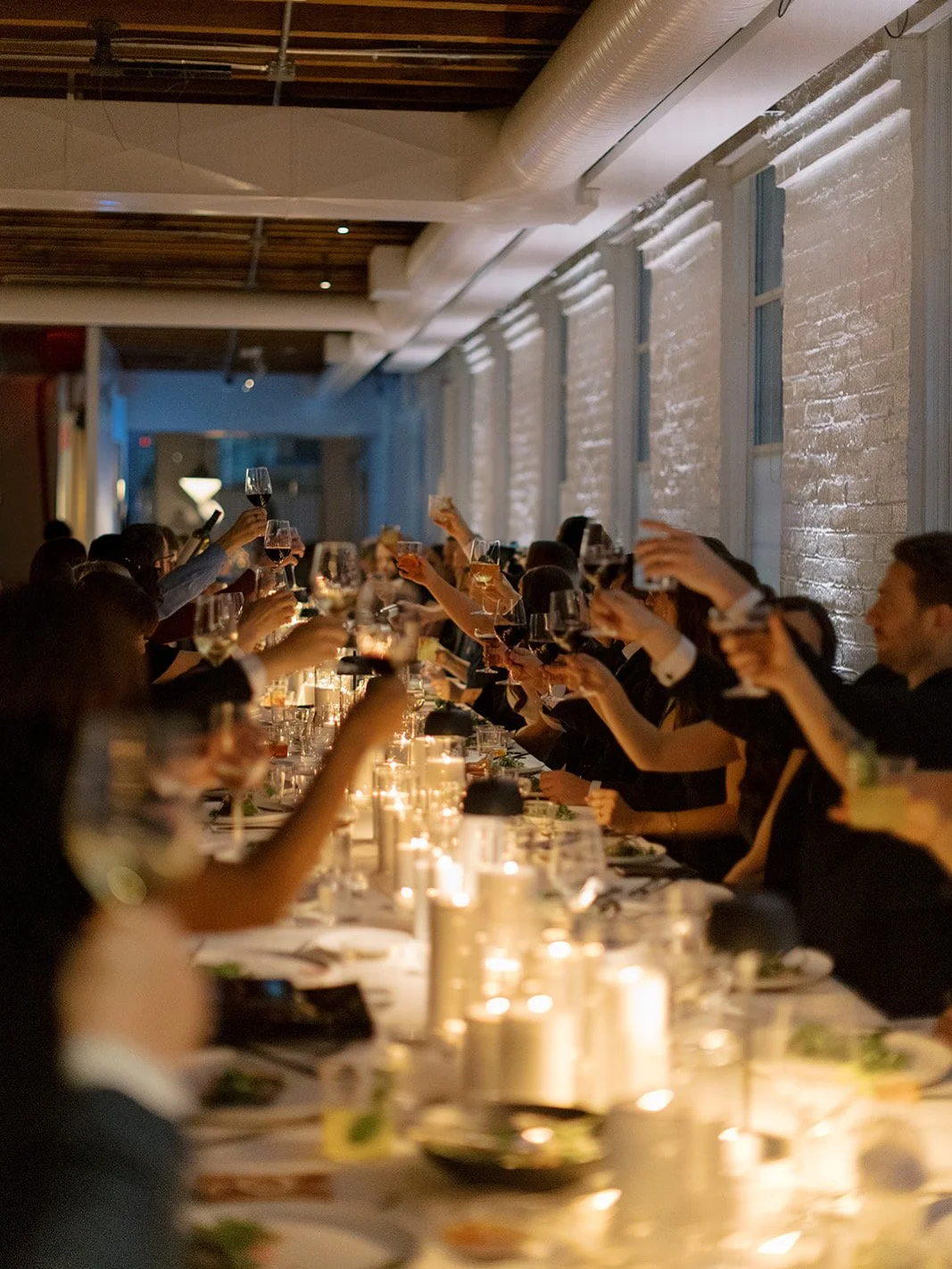 People at a formal dinner celebration raising glasses in a toast inside a warmly lit room with candles on the table. Sweetheart Events | Christine Pienaar Photography | The Kent Venue