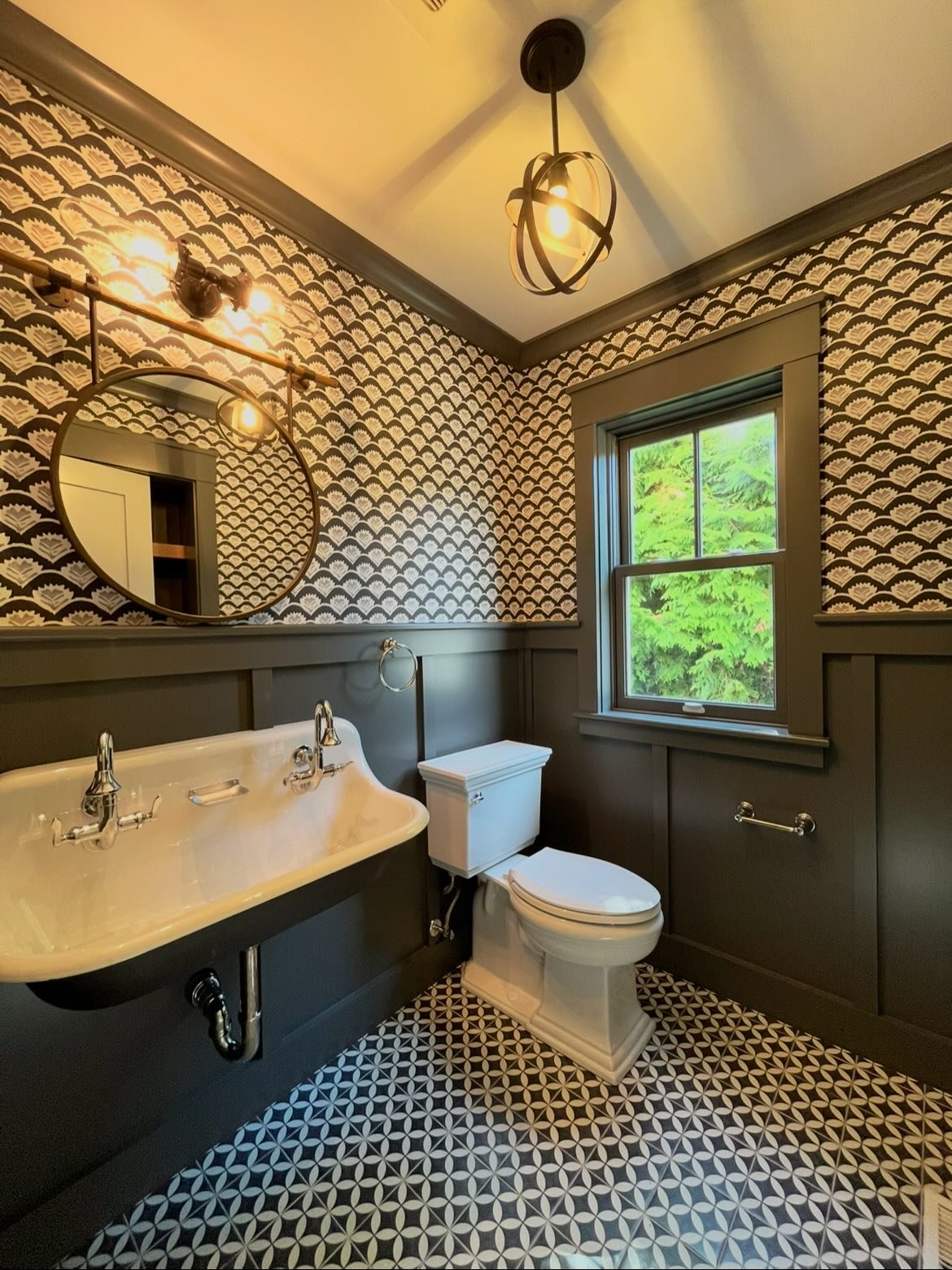 Small space. Big statement.

This powder room was all about contrast and detail&mdash;moody paneled walls paired with a bold patterned floor and wallpaper that ties it all together. The warm wood shelving adds just enough balance to keep it from feel