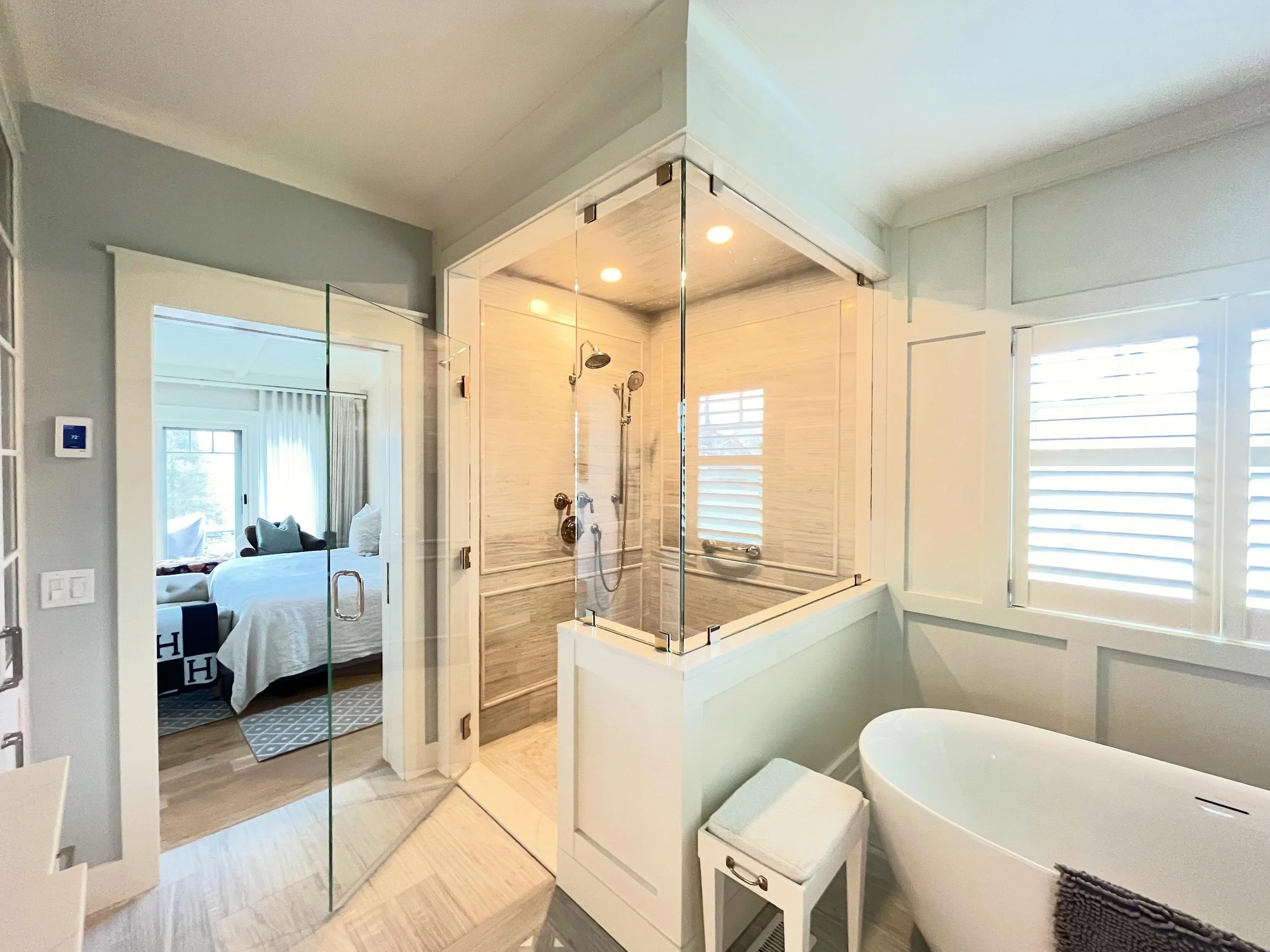 A primary bathroom designed to feel calm, bright, and timeless.

Custom wall paneling, a freestanding soaking tub, and a glass-enclosed shower layered with soft textures and clean lines throughout. Spaces like this are all about balance&mdash;warmth,