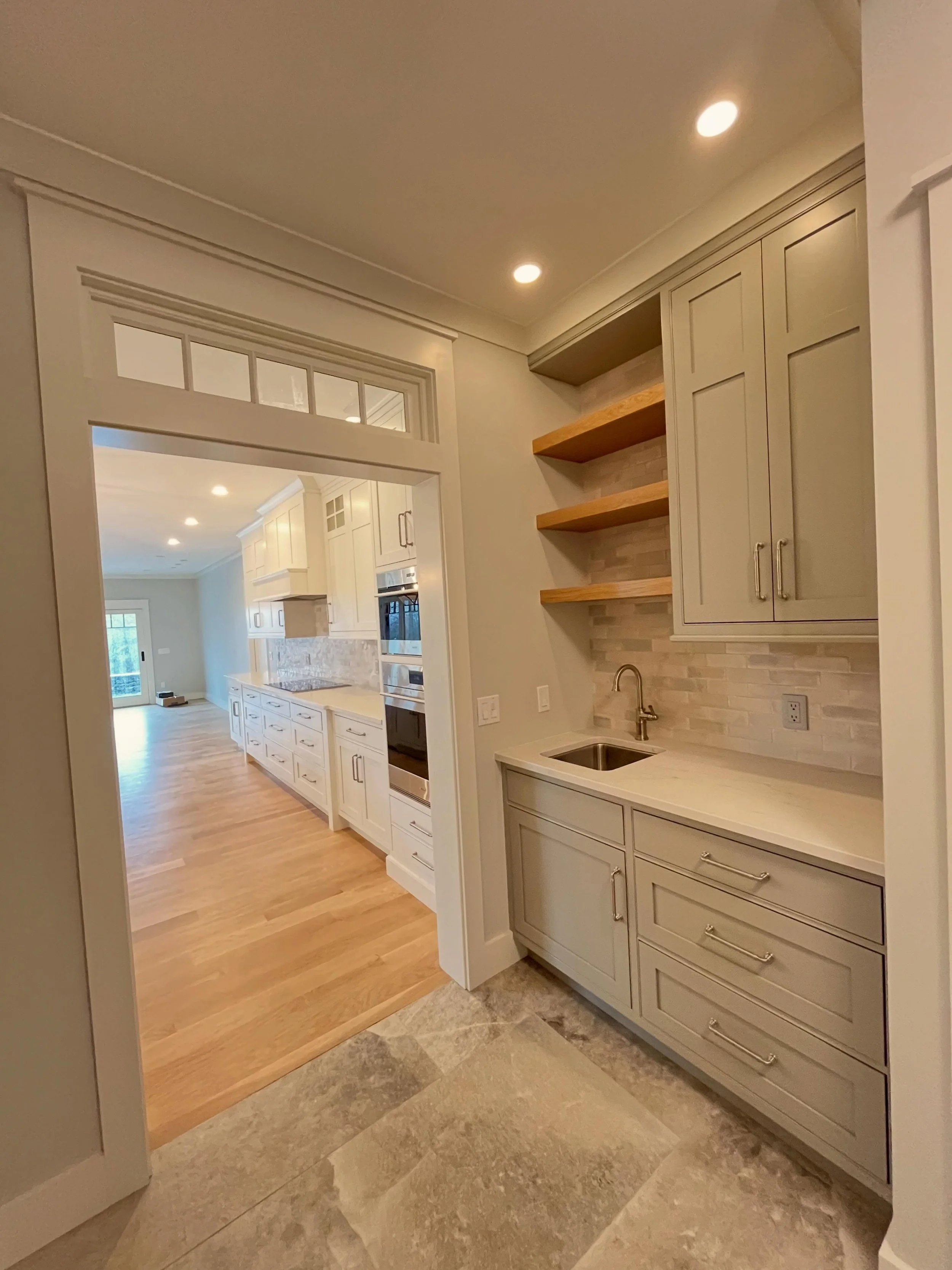 A seamless transition into the heart of the home. This custom coffee bar pairs warm white oak shelving, layered textures, and tailored cabinetry with a transomed cased opening that keeps the kitchen feeling open, connected, and full of natural flow. 