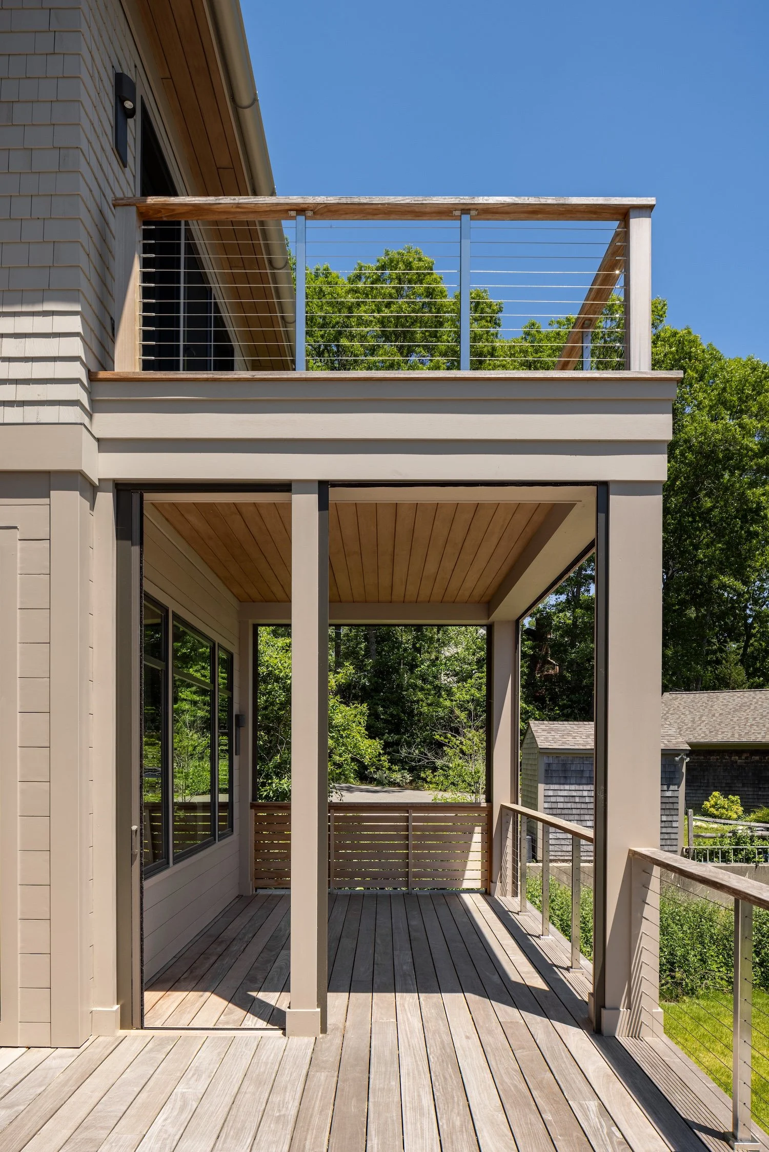 Covered outdoor deck with cedar ceiling, cable railings, and upper balcony on a luxury Rhode Island custom home.