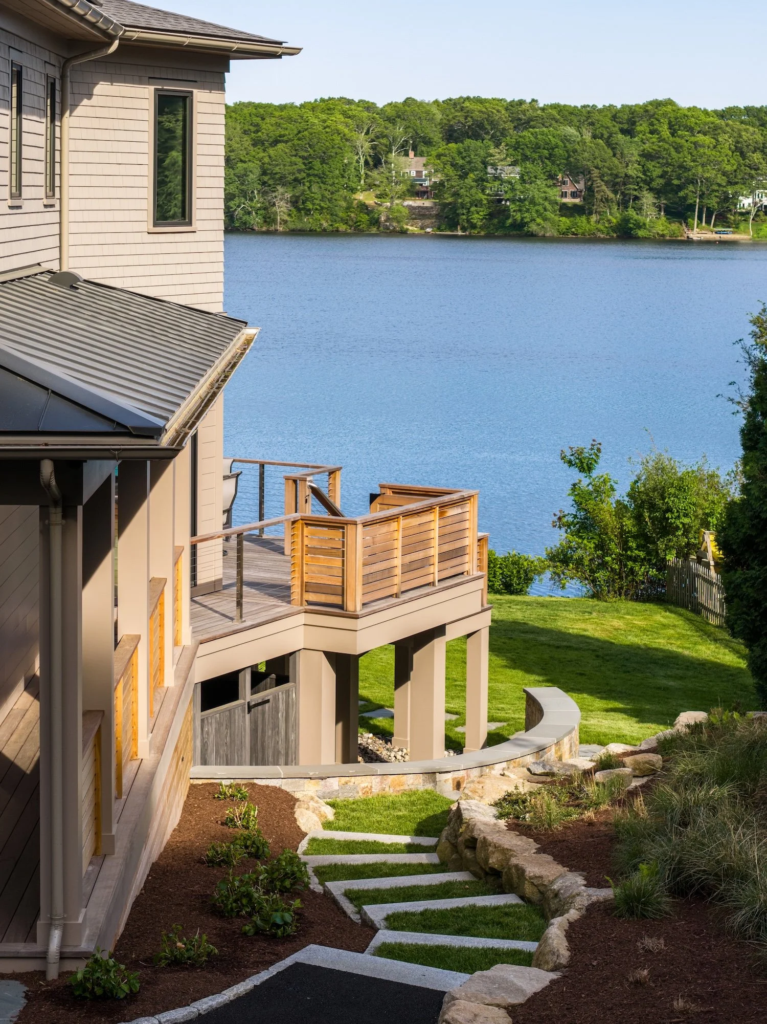 Luxury waterfront custom home with multi-level decks, landscaped stone steps, and outdoor living spaces overlooking the water.
