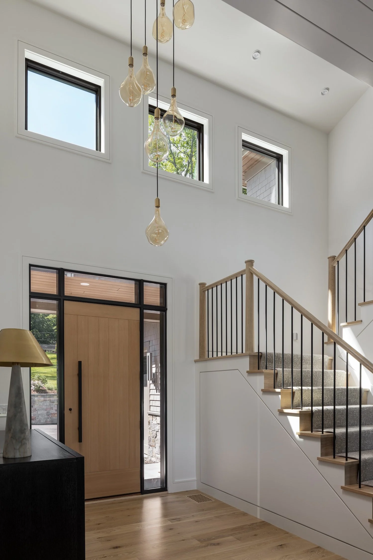 Grand foyer featuring a custom white oak front door, open staircase, and designer lighting in a luxury Rhode Island custom home.