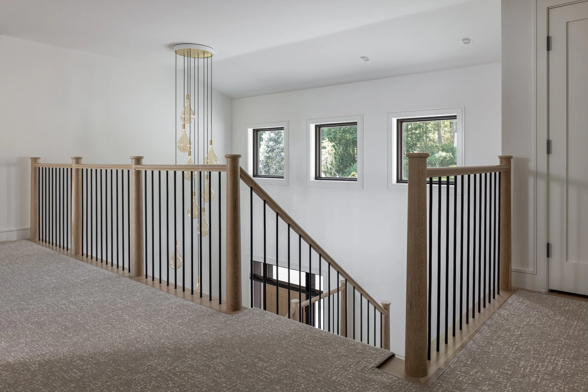 Modern open staircase with white oak railings, black metal balusters, and a contemporary pendant light in a luxury custom home.