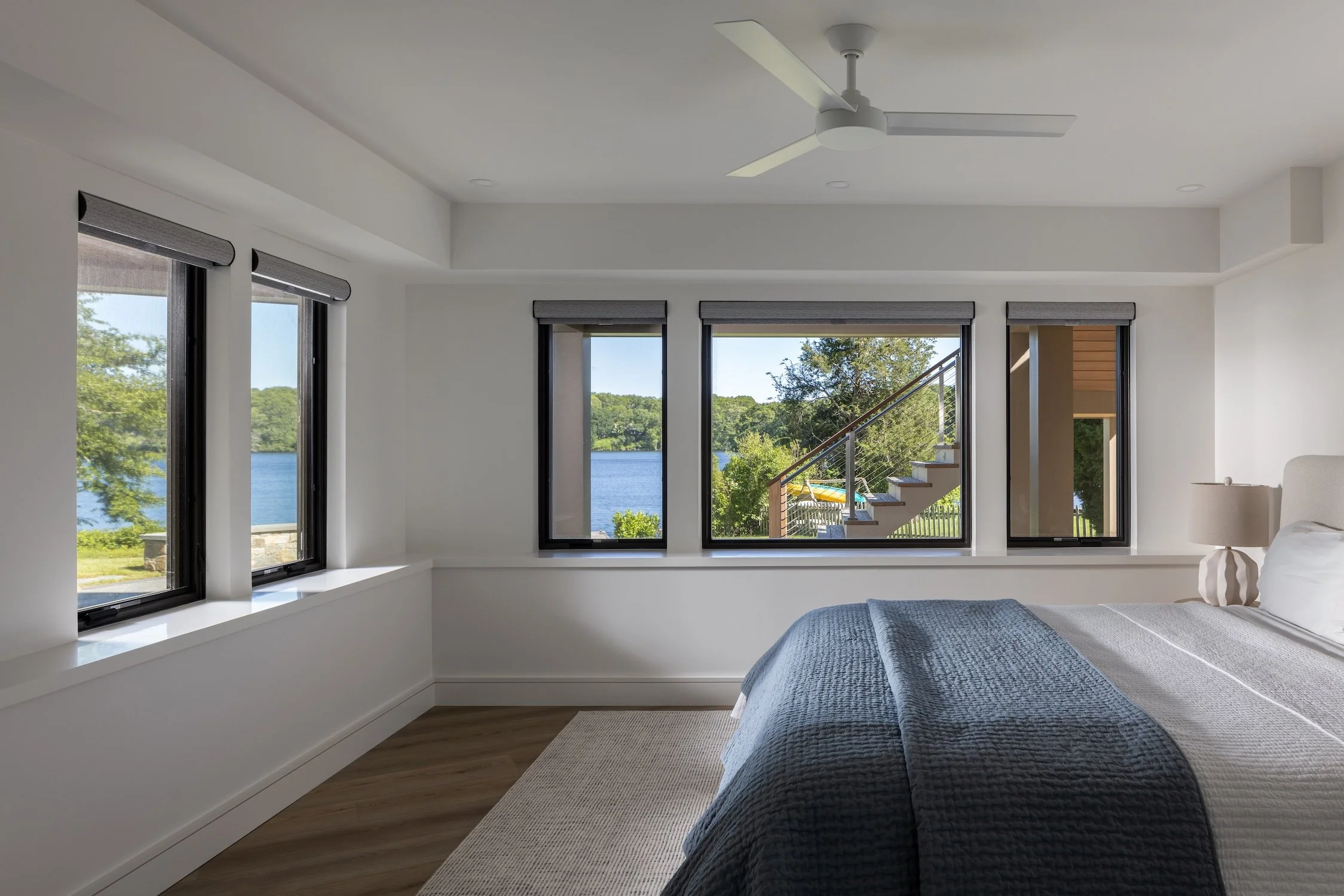 Bright waterfront bedroom with large picture windows, modern finishes, and expansive water views in a luxury custom home.