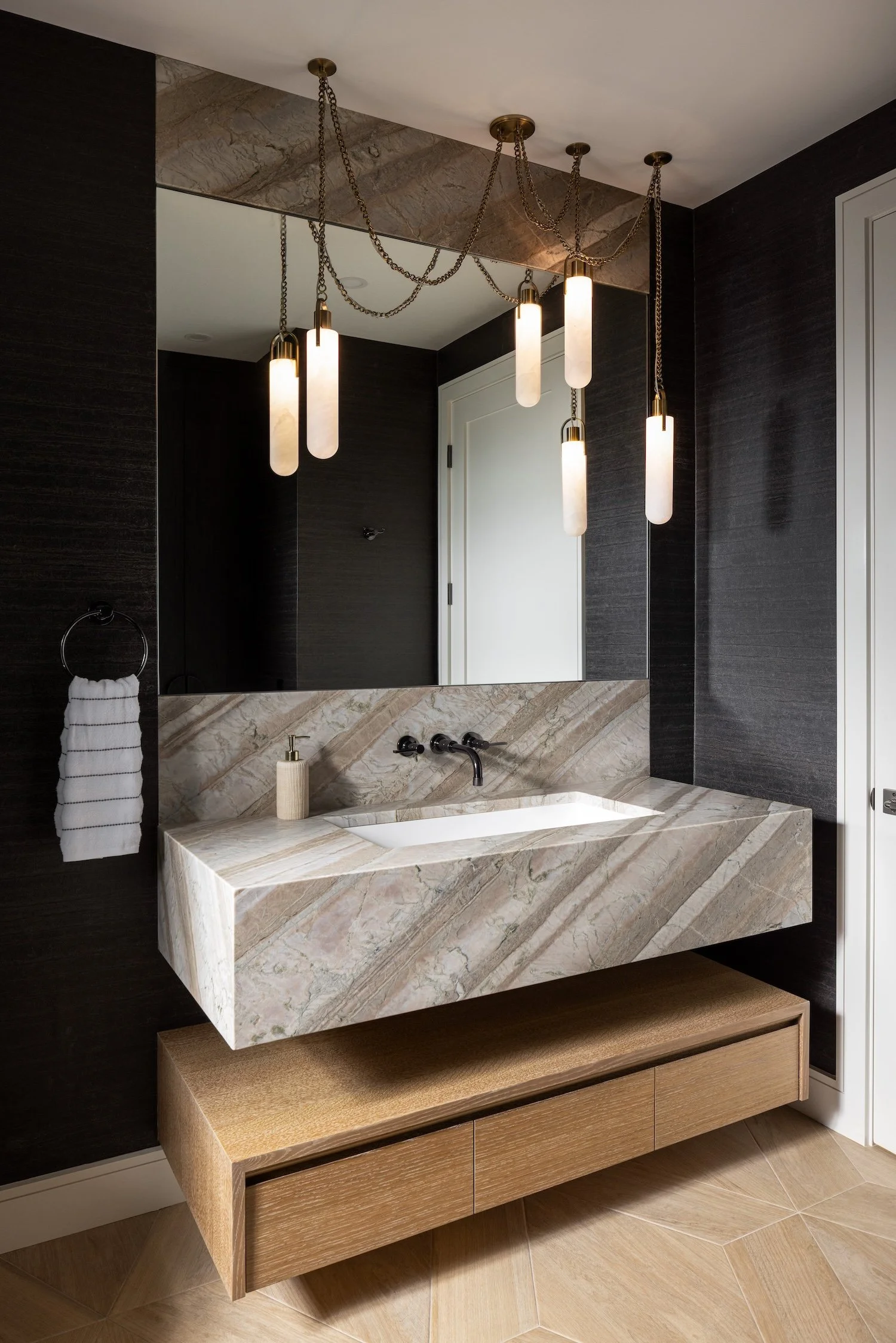 Luxury powder room with a floating natural stone vanity, custom wood cabinetry, designer pendant lighting, and textured wallcovering.