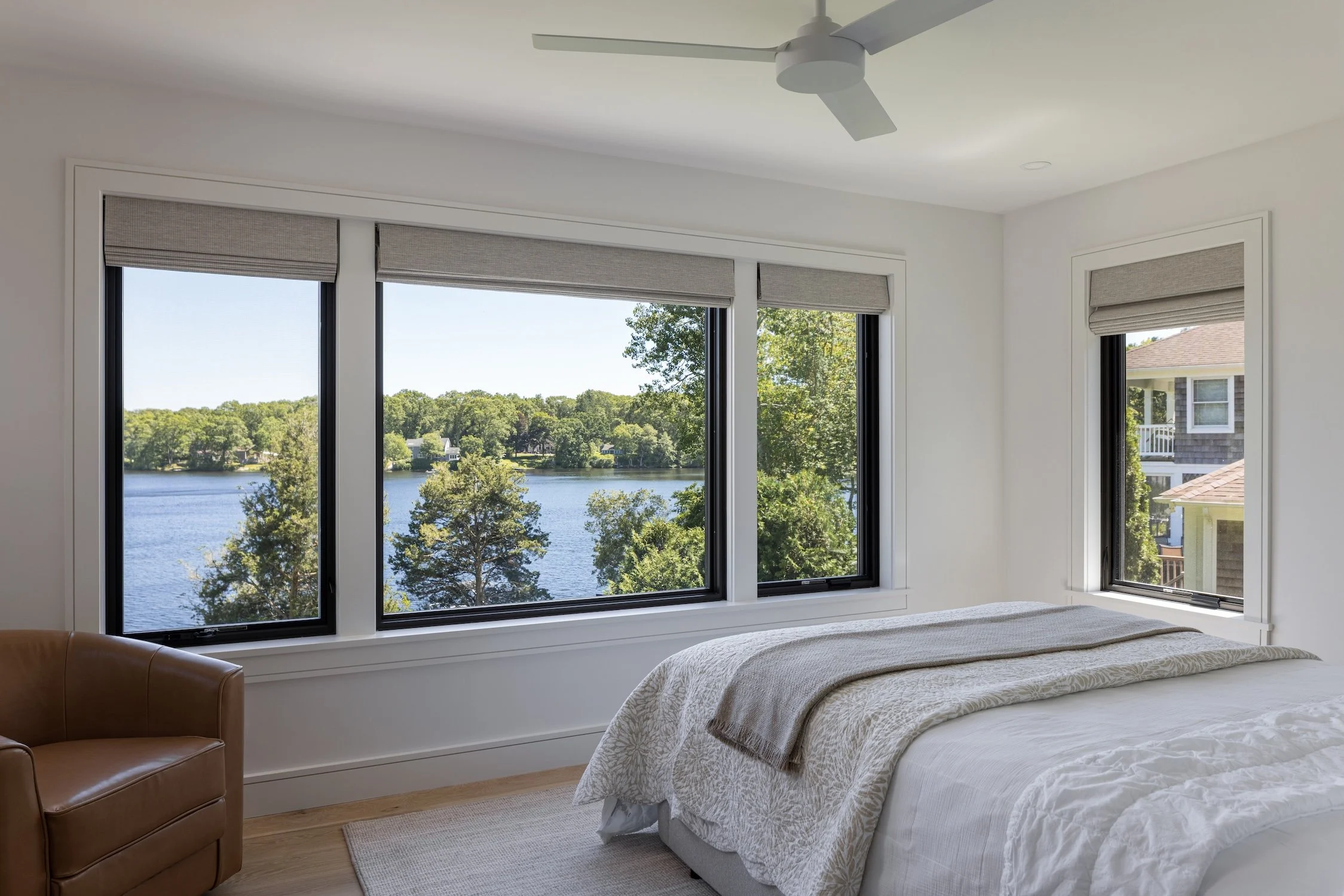 Bright waterfront bedroom with large picture windows, modern finishes, and expansive water views in a luxury custom home.