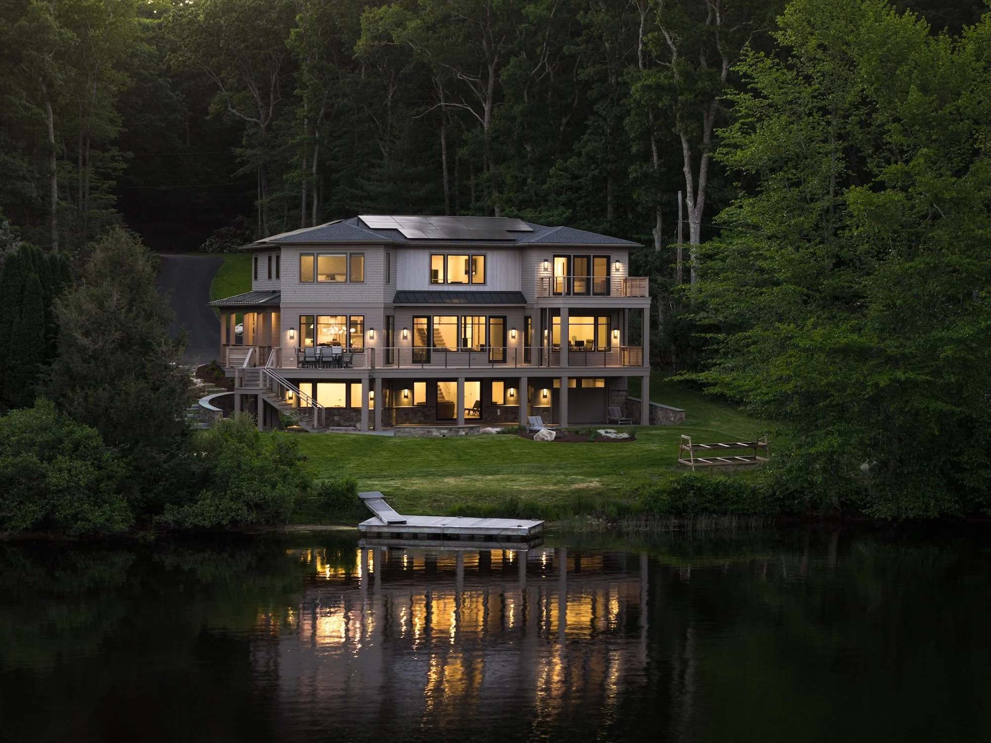 Luxury waterfront custom home at twilight with expansive outdoor living spaces, private dock, and illuminated modern coastal architecture.