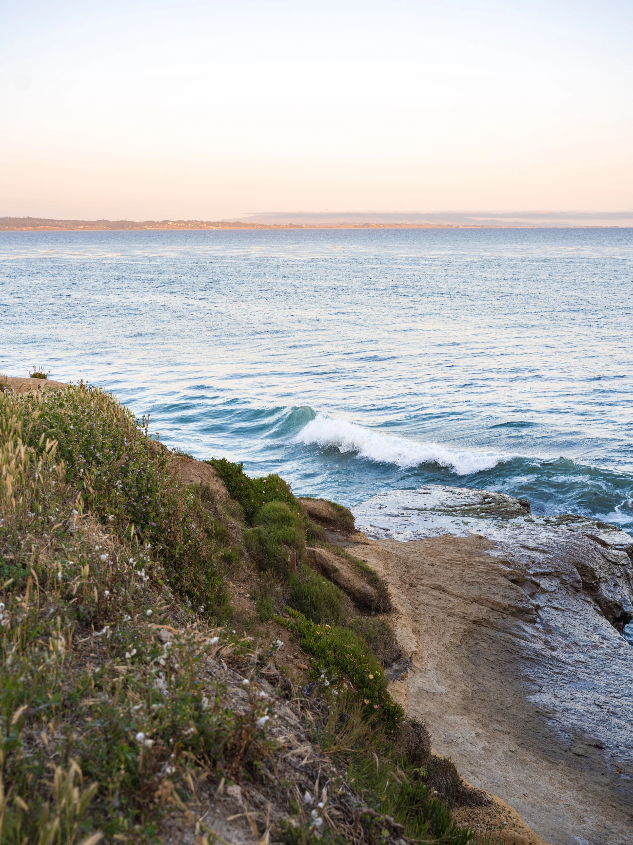 Coastal scene with rocky shore, waves, and calm ocean under clear sky
