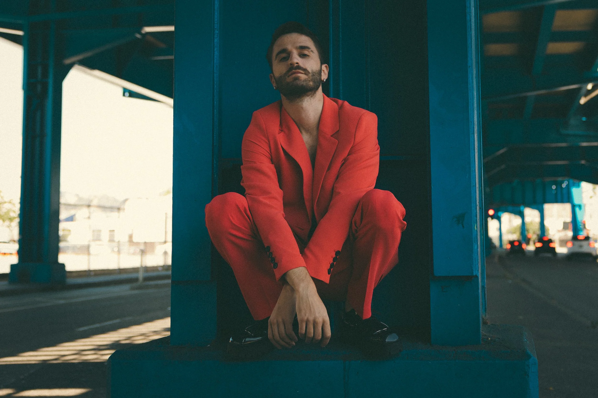 Man in a red suit sitting on a concrete ledge under the Central Freeway Viaduct, with traffic lights and vehicles in the background.