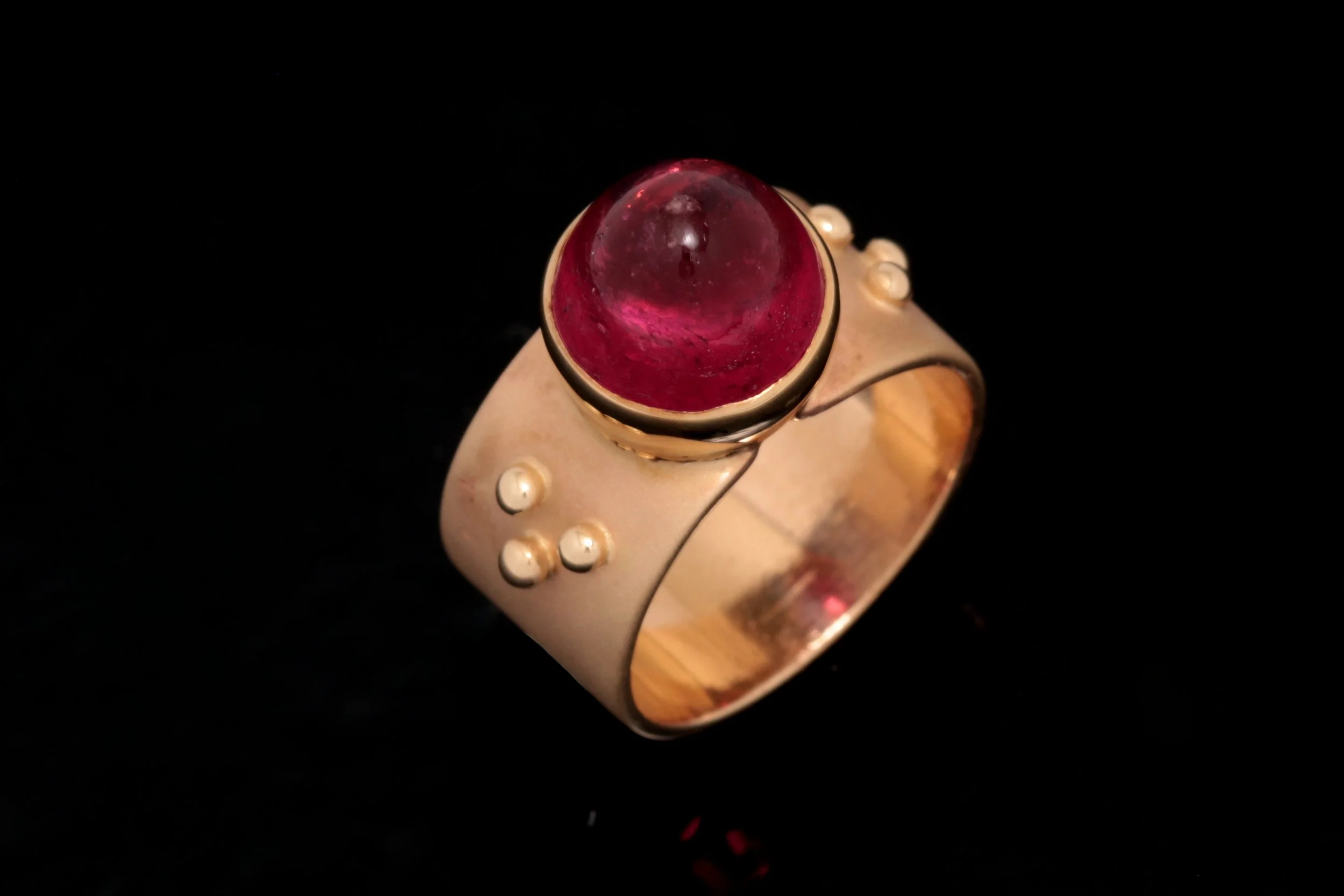 Rubellite Tourmaline Cabochon Ring
Showcasing a high-dome rubellite tourmaline cabochon from the Legacy collection, this striking ring is set on a textured flat band with intricate glass bead-like detailing and large granules. The bold yet refined de