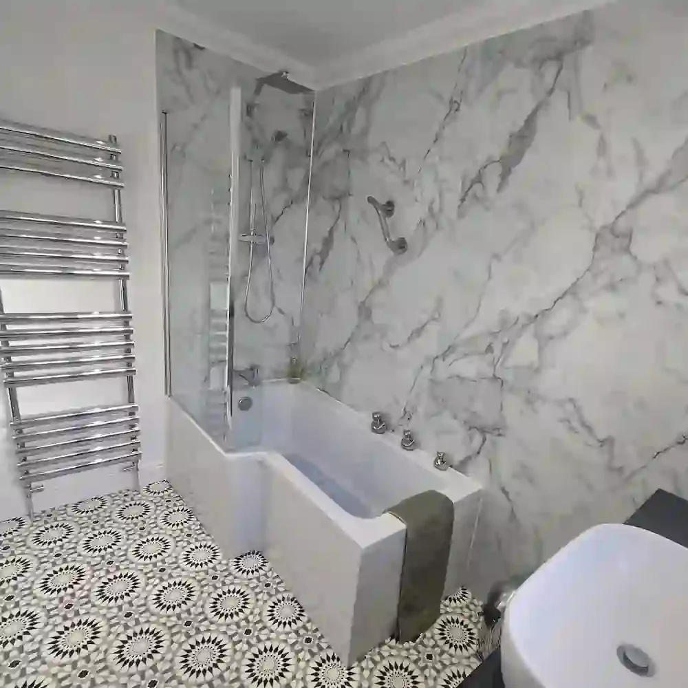 A stunning modern bathroom installation completed by Eastside Gas LTD in Lowestoft. The newly fitted bathroom features an L-shaped shower bath with a glass screen, elegant marble-effect wall panels, a large chrome heated towel rail, geometric floor