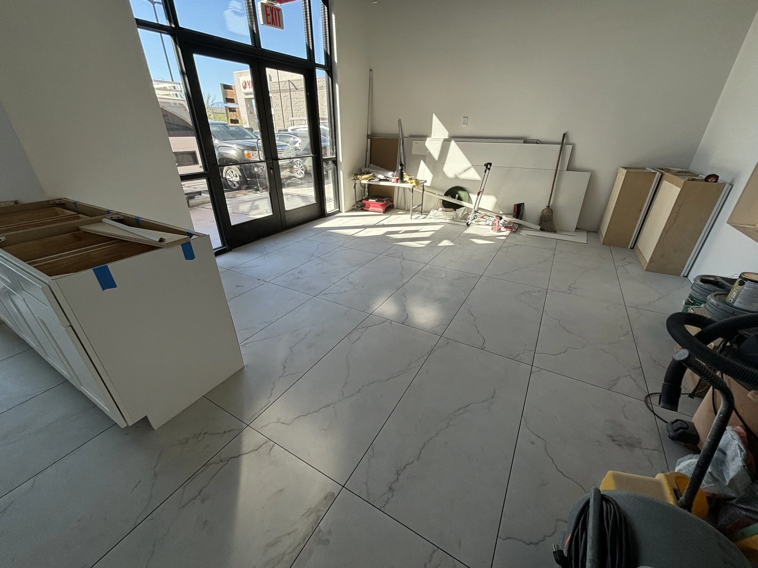 Empty room with tiled floor, partially installed white cabinets, and construction tools and materials.