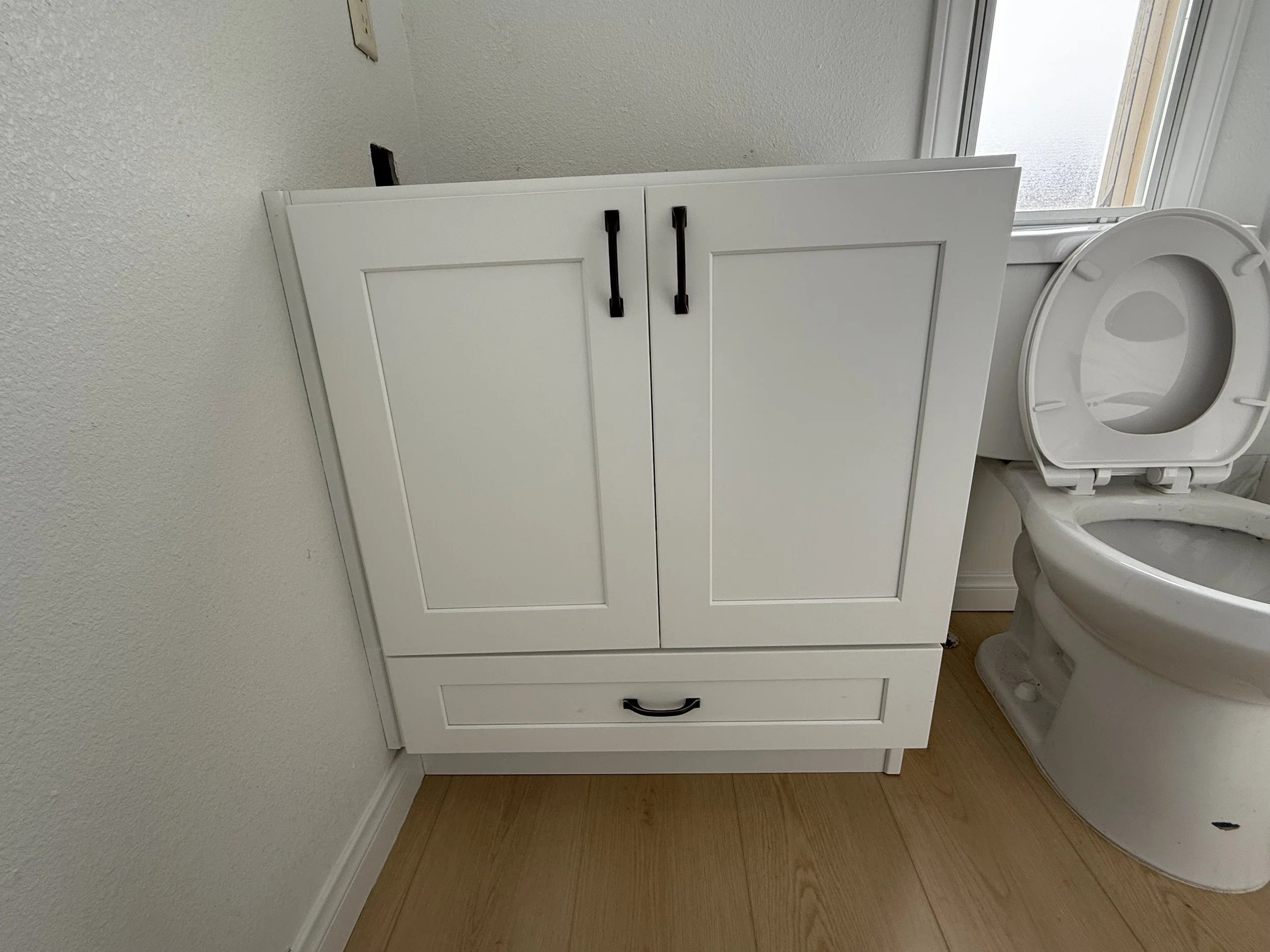 Bathroom with white vanity cabinet and open toilet with wooden floor