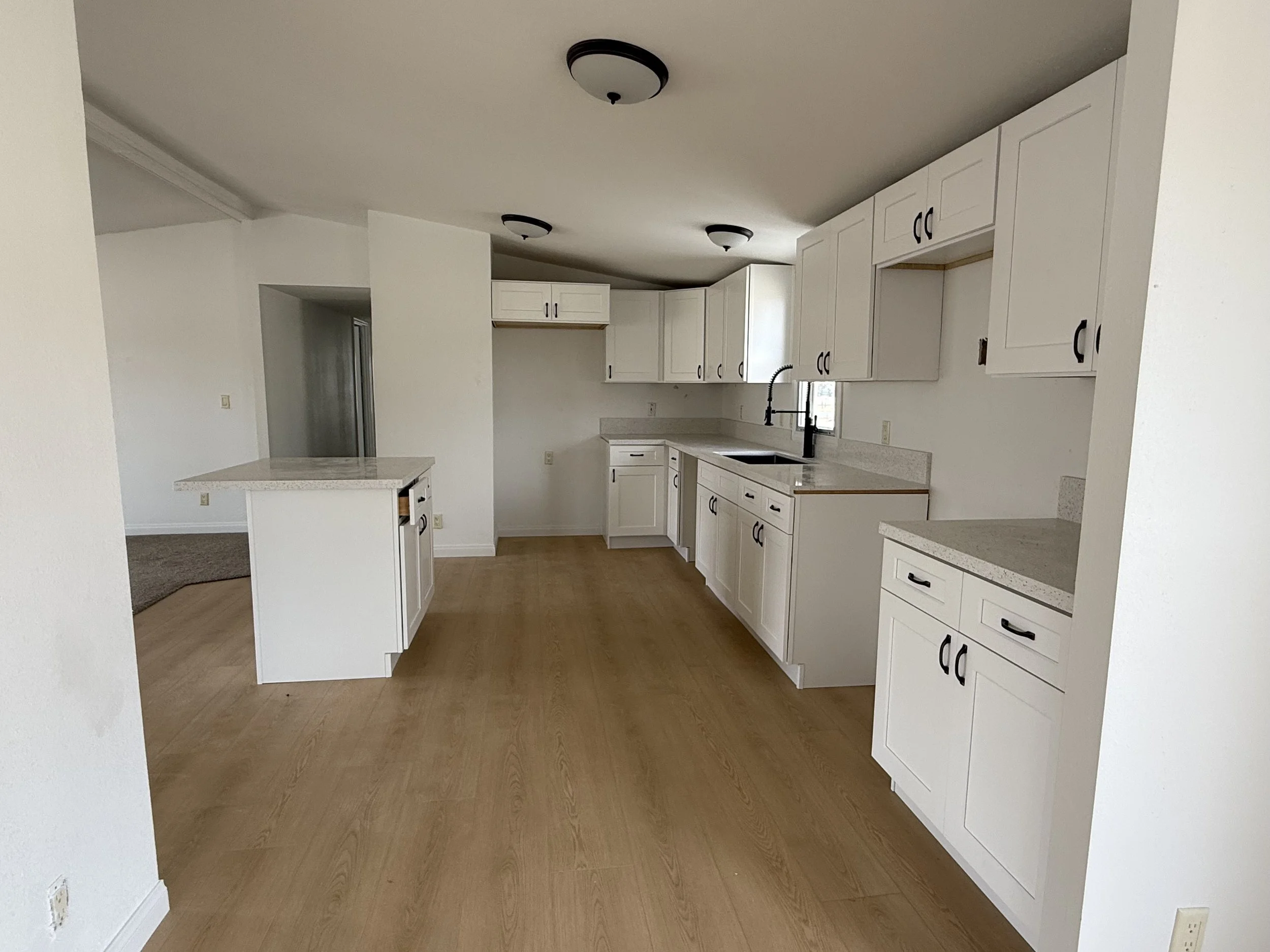 Modern kitchen with white cabinets, wood flooring, a central island, and black faucets.