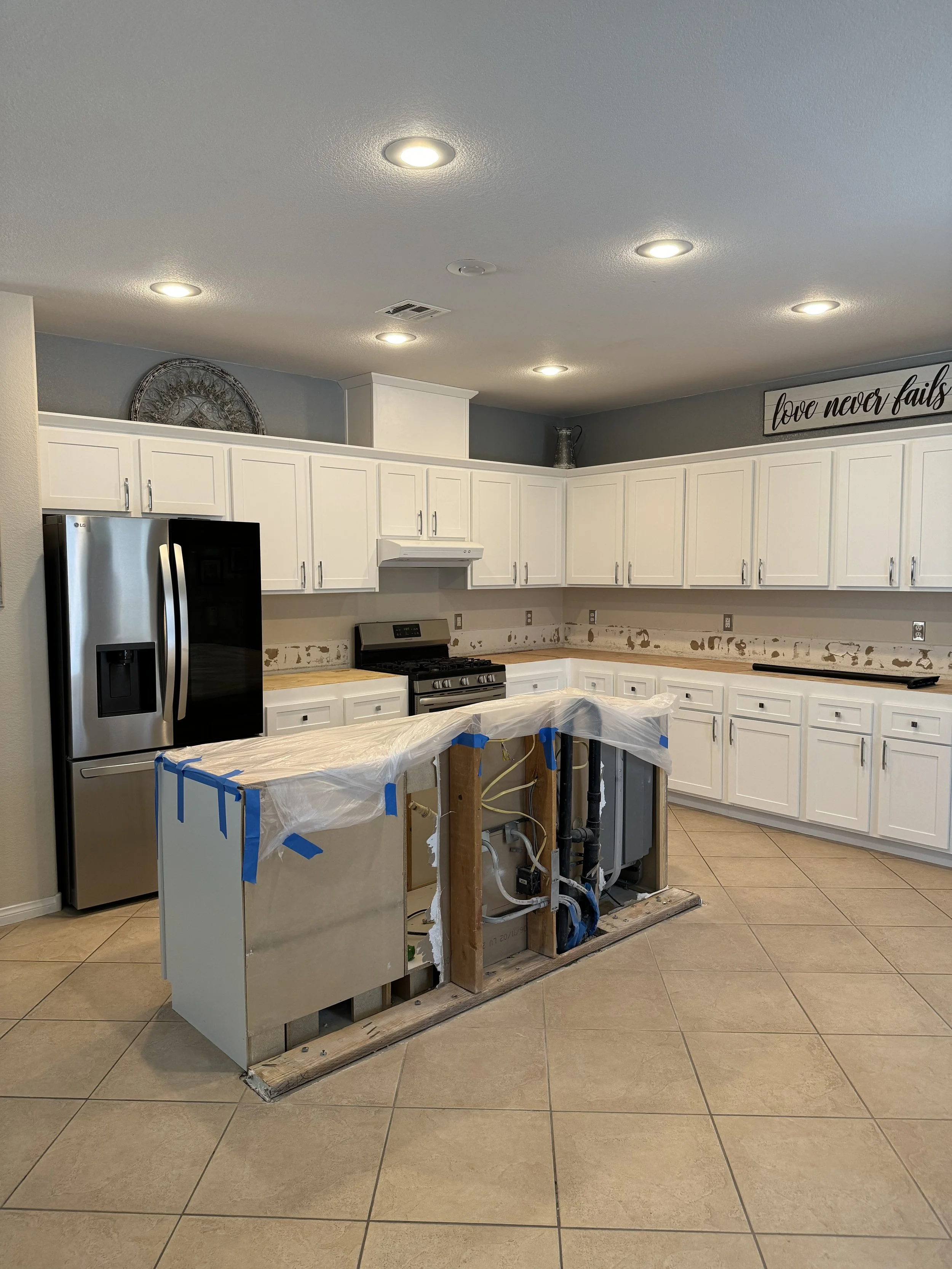 Kitchen under renovation with white cabinets, recessed lighting, a partially constructed island with exposed plumbing, stainless steel appliances, and tiled flooring.