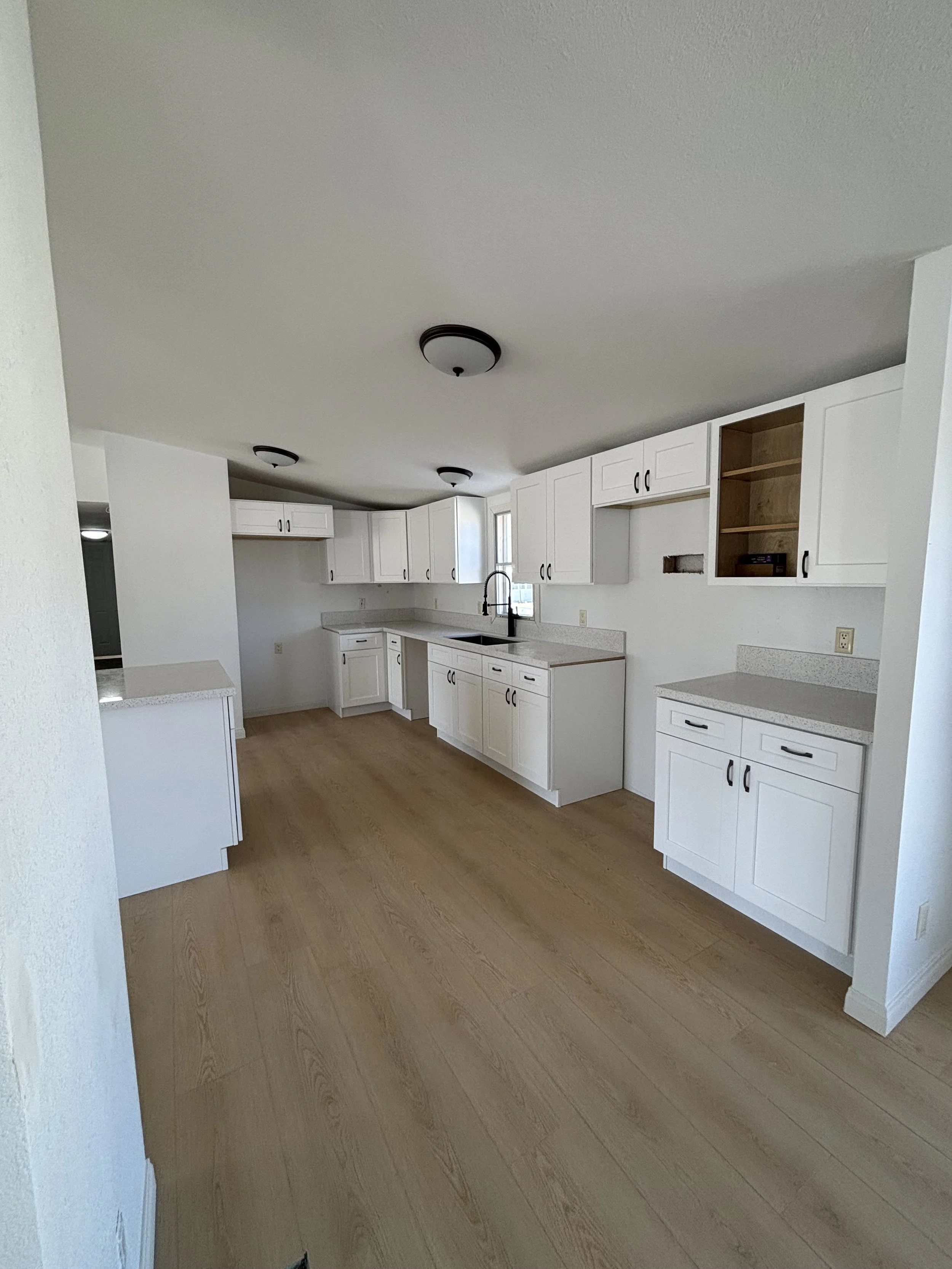 Modern kitchen with white cabinets, light wood flooring, and simple black light fixtures