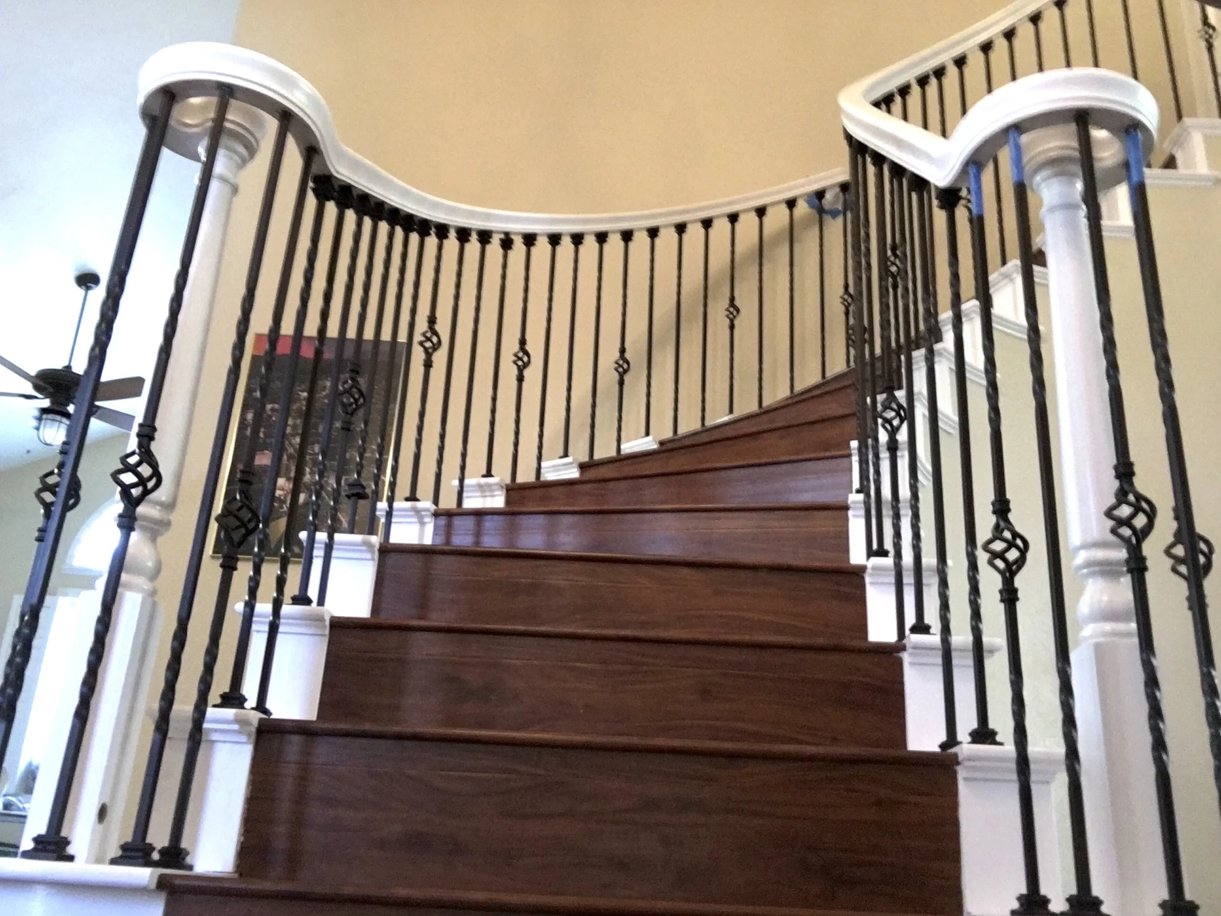 Curved wooden staircase with ornate black metal balusters and white handrails.