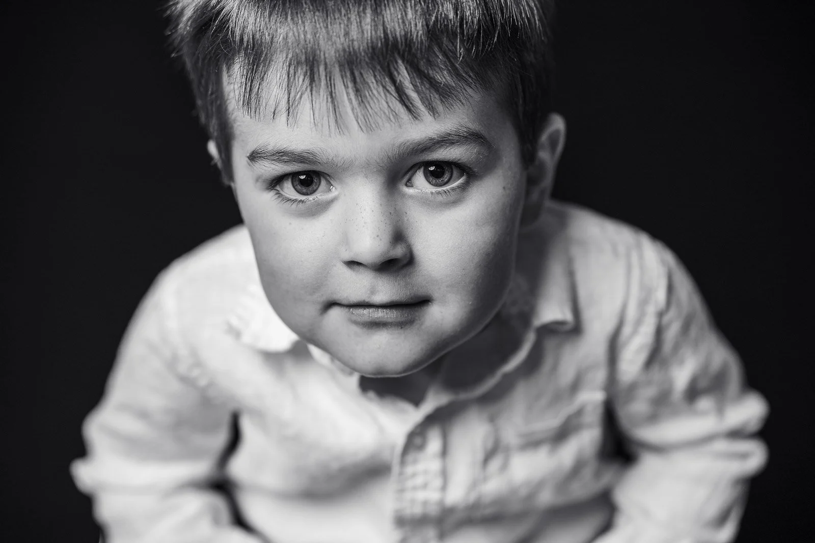 Black and white close-up portrait of a young boy with expressive eyes, looking directly at the camera, wearing a collared shirt.