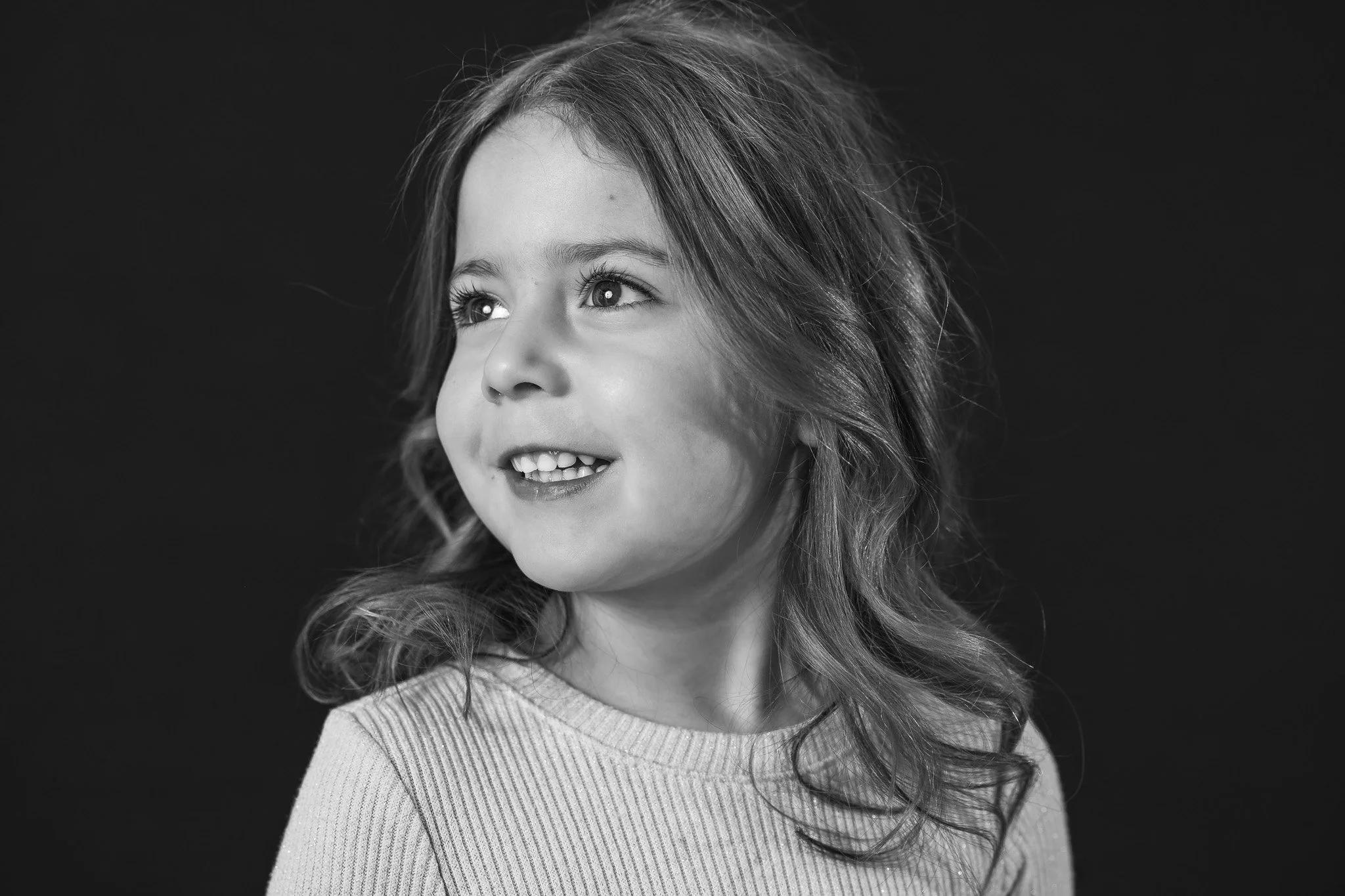 Black and white portrait of a young girl with curly hair, looking to the side and smiling.