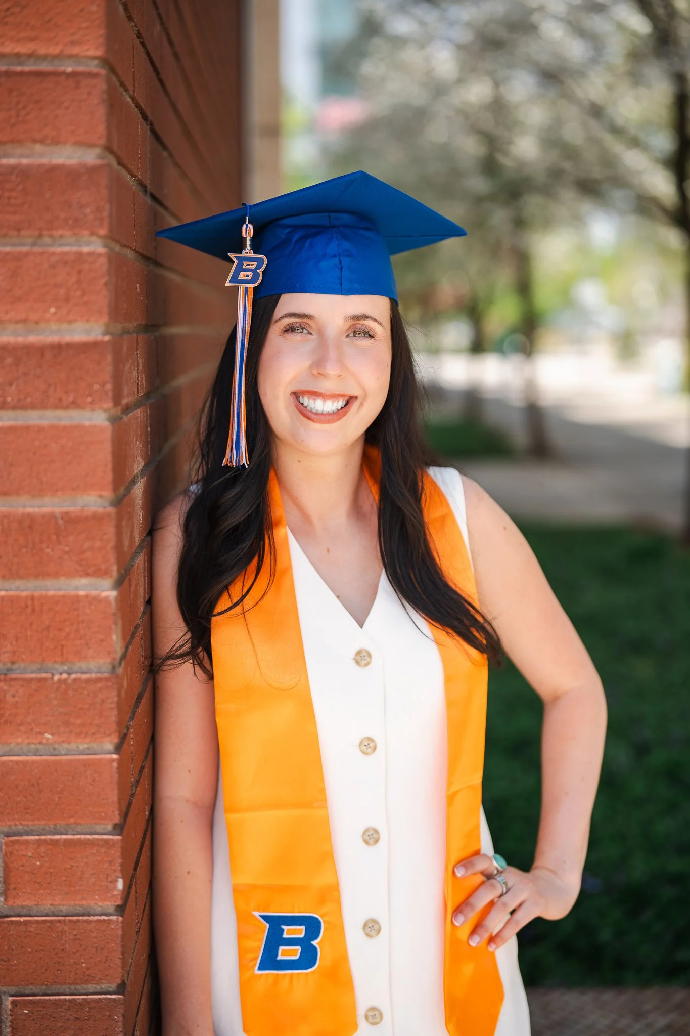 Outdoor graduation photo near Boise State featuring a smiling senior in a blue cap and orange stole. Fun and confident grad portraits for Boise, Eagle, Star, Meridian, and the Treasure Valley.