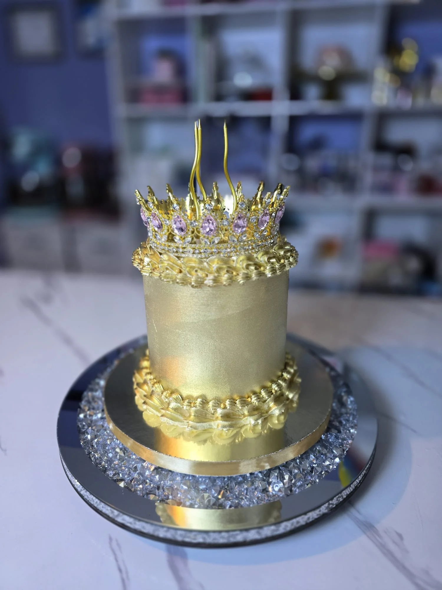 Pastel de cumpleaños dorado con corona decorativa y base de espejo y cristal
