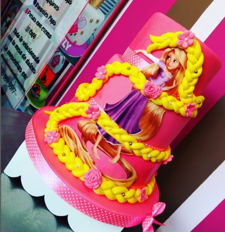 Pastel de cumpleaños con temática de Rapunzel, decorado con cabello largo y trenza de color amarillo, rosas y flores, en tonos rosados y morados.