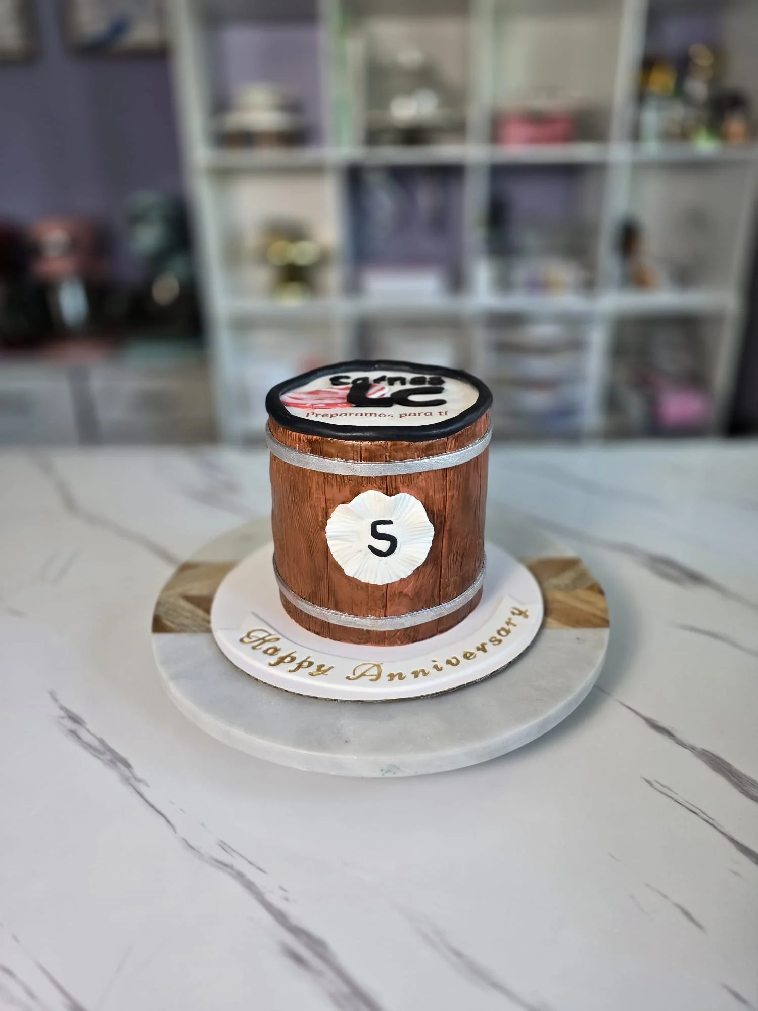 Pastel con forma de barril de madera con la letra 'S' y mensaje de felicitación en la base que dice 'Feliz Aniversario'.