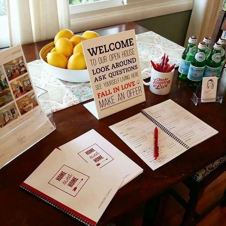 A table set up for a home tour event with a bowl of lemons, a sign welcoming visitors, bottled water, and informational booklets.